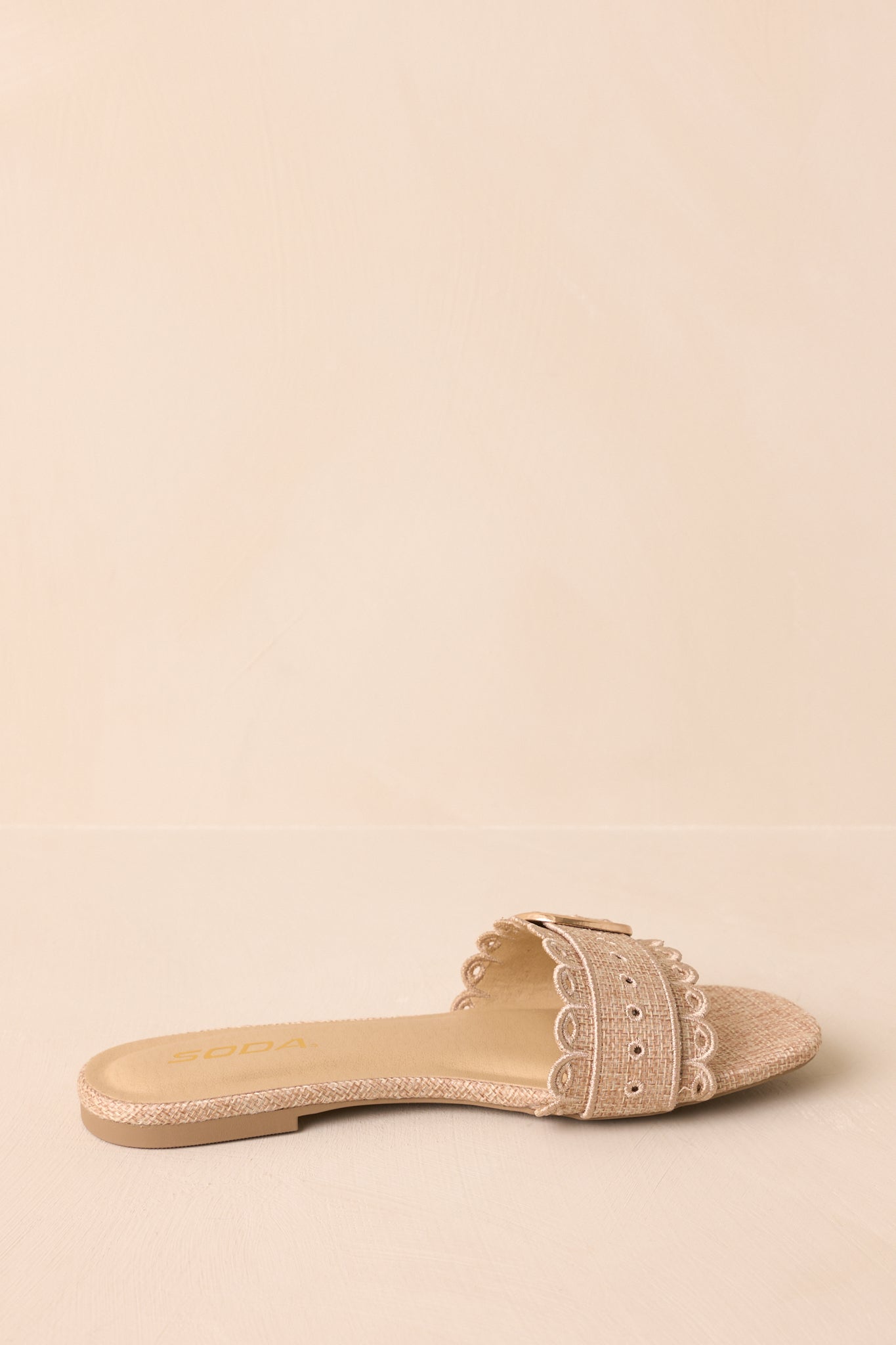 Natural woven flat sandals with scalloped trim captured at an angled view against beige.