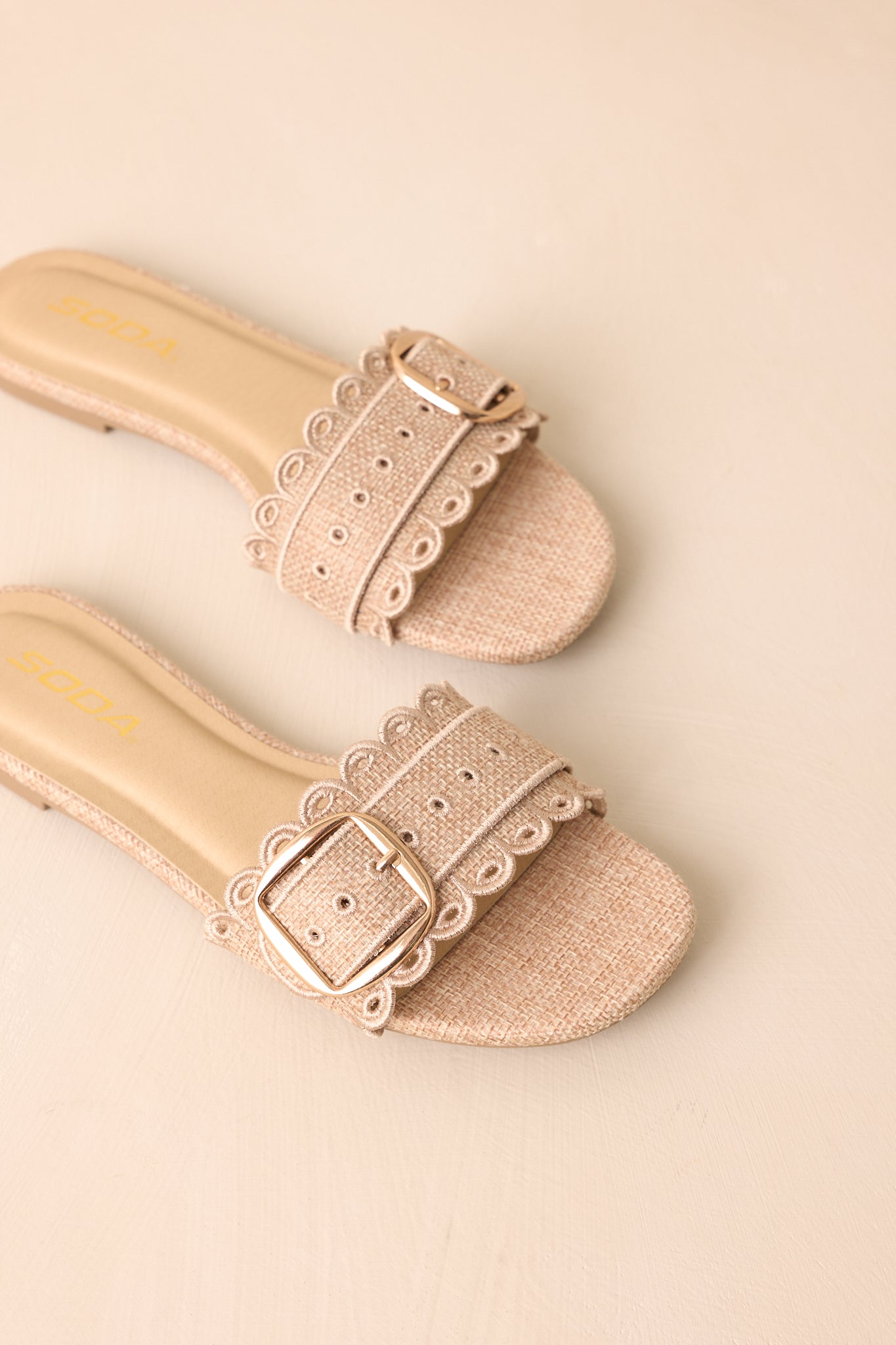 Slip-on woven sandals featuring embroidered eyelets and decorative buckle displayed from above.