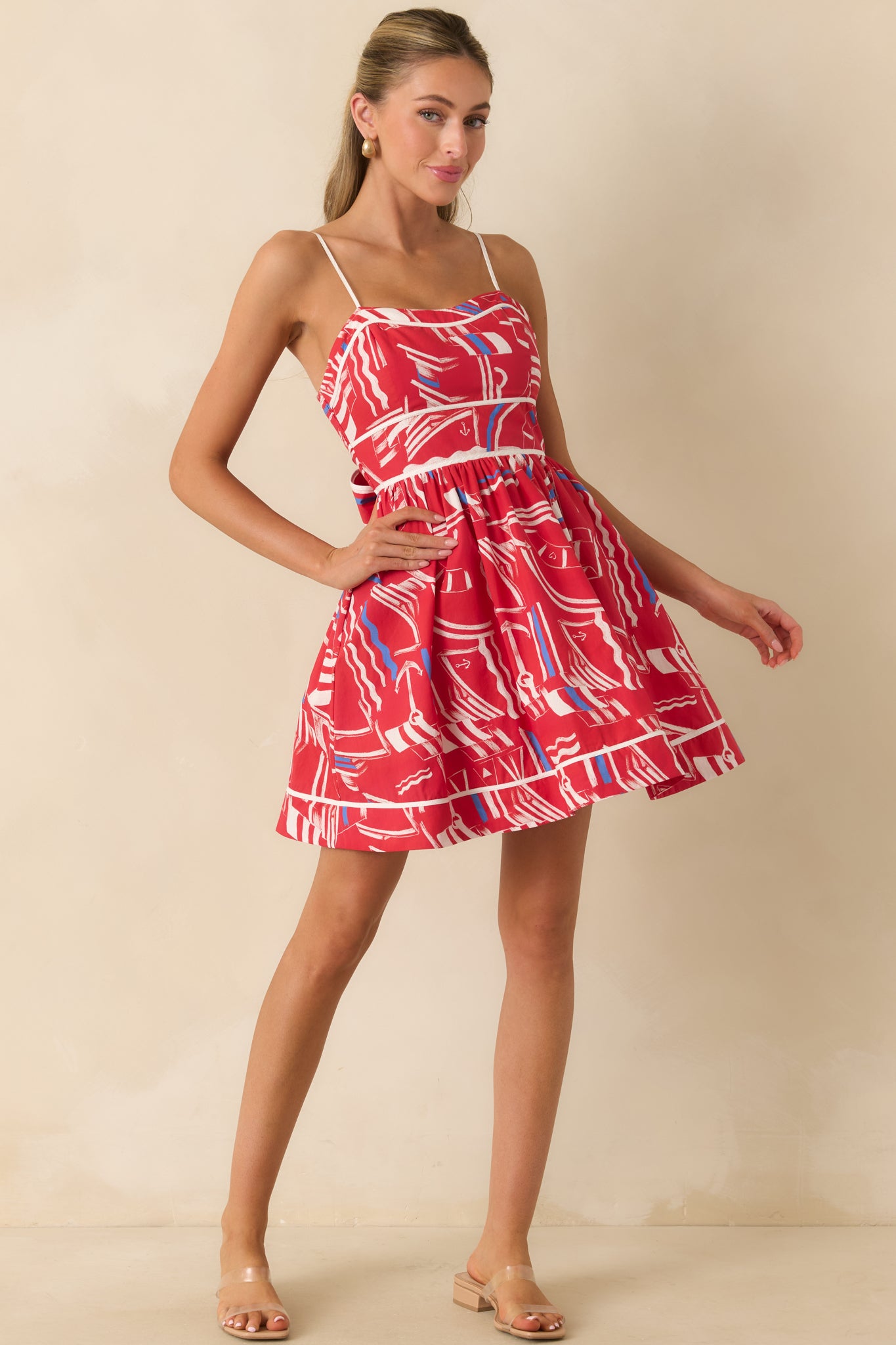 Cotton mini dress featuring a sweetheart neckline, adjustable spaghetti straps, contrast piping, yacht club print, and gathered skirt.