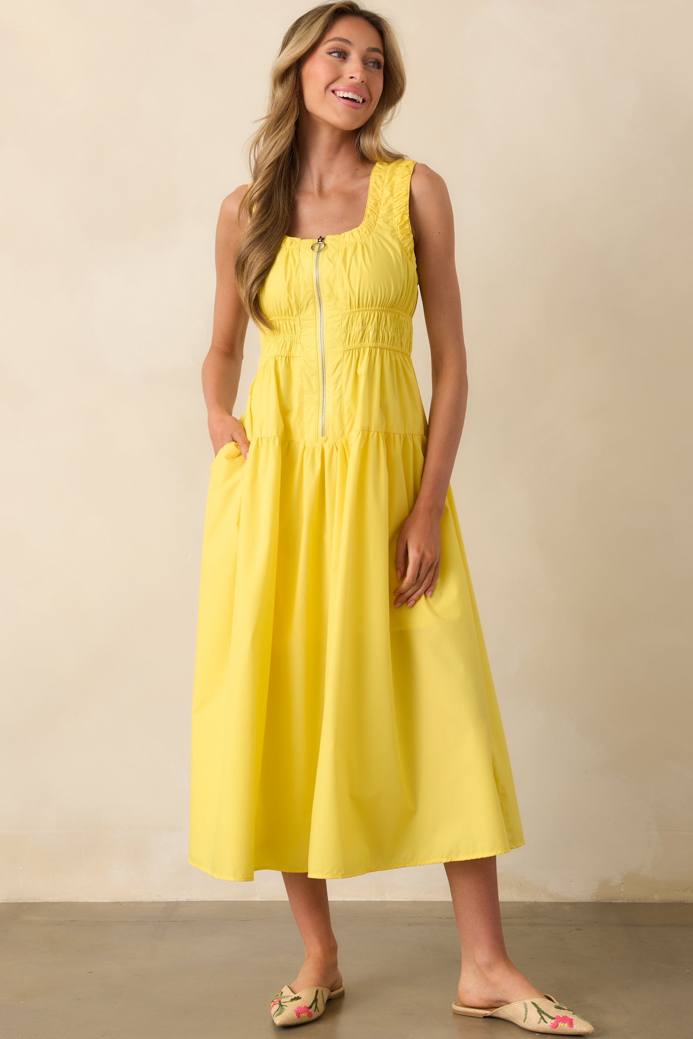 Frontal image of a yellow midi-length dress, featuring a zippered front with an o-ring detail and gathered waistline for a cinched silhouette.