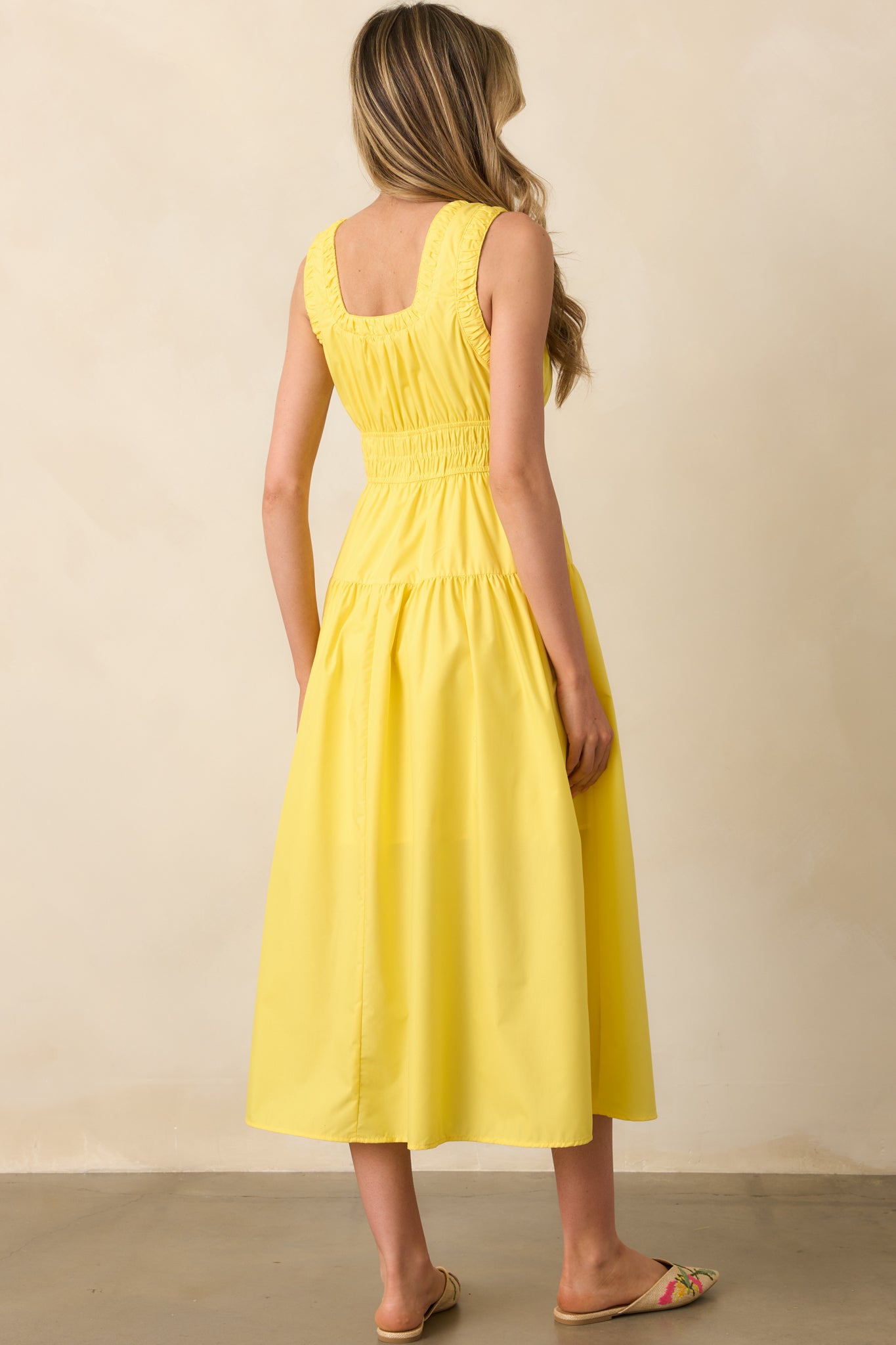 A view from behind of the yellow midi dress, revealing its sleeveless cut and gathered waistline without visible fastenings.