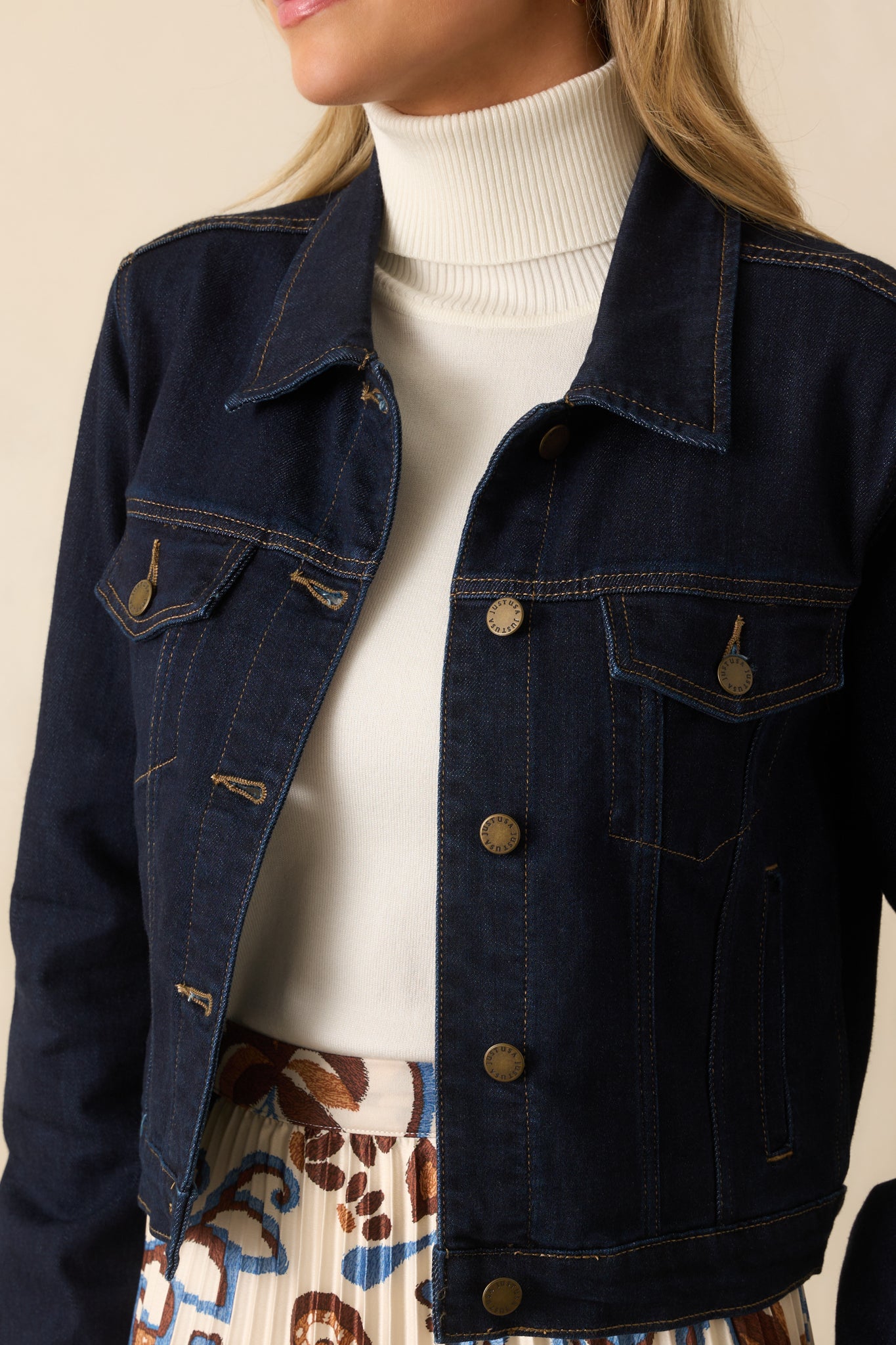 Zoomed detail of the denim jacket’s textured dark wash fabric and contrast stitching.