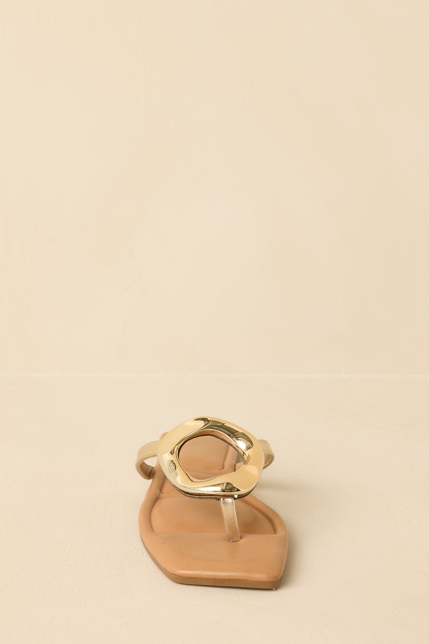 Zoomed-in image of the gold flat sandals emphasizing the statement gold-tone ring accent at the vamp.