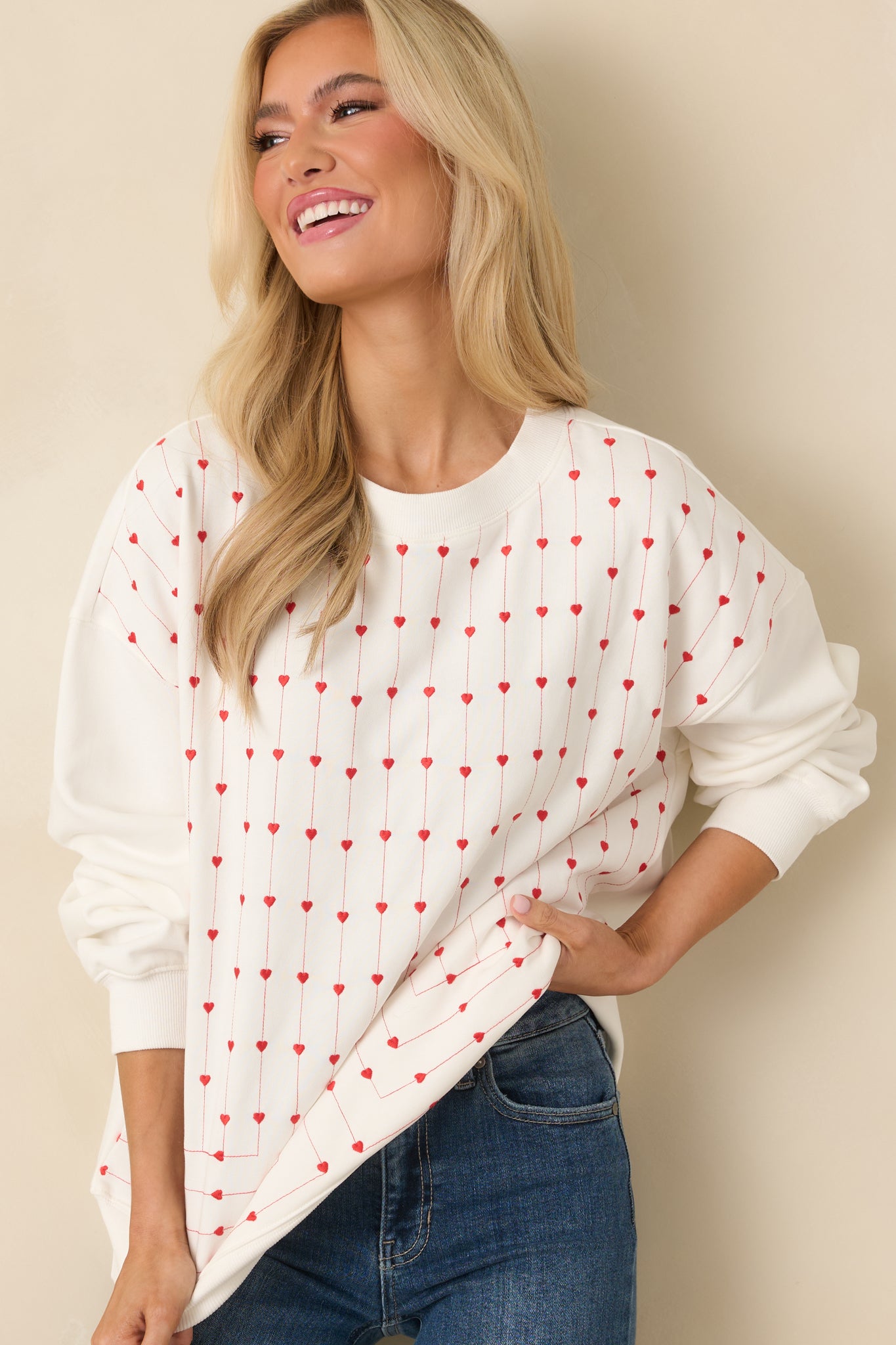 Zoomed view of the white cotton sweatshirt’s front heart embroidery, showing tight vertical rows of raised stitched hearts on the soft knit fabric.