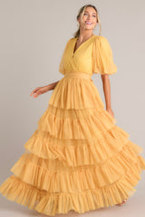 Angled full body view of this yellow dress features a v-neckline, puff sleeves, elastic stretch around the waist, a removable self-tie at the waist, and a tiered flowy skirt.