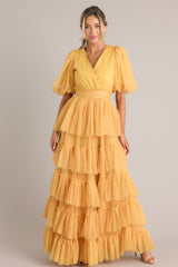 Front view of this yellow dress features a v-neckline, puff sleeves, elastic stretch around the waist, a removable self-tie at the waist, and a tiered flowy skirt.