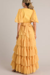 Back view of this yellow dress features a v-neckline, puff sleeves, elastic stretch around the waist, a removable self-tie at the waist, and a tiered flowy skirt.