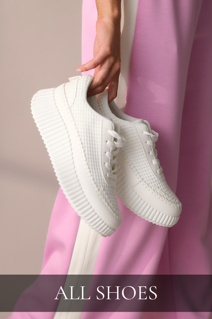 Woman holding white platform sneakers styled with pink wide-leg pants, linking to the All Shoes shop.