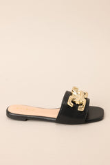 Side view of these black flat sandals that feature a slip on style, and a large gold buckle-like design.