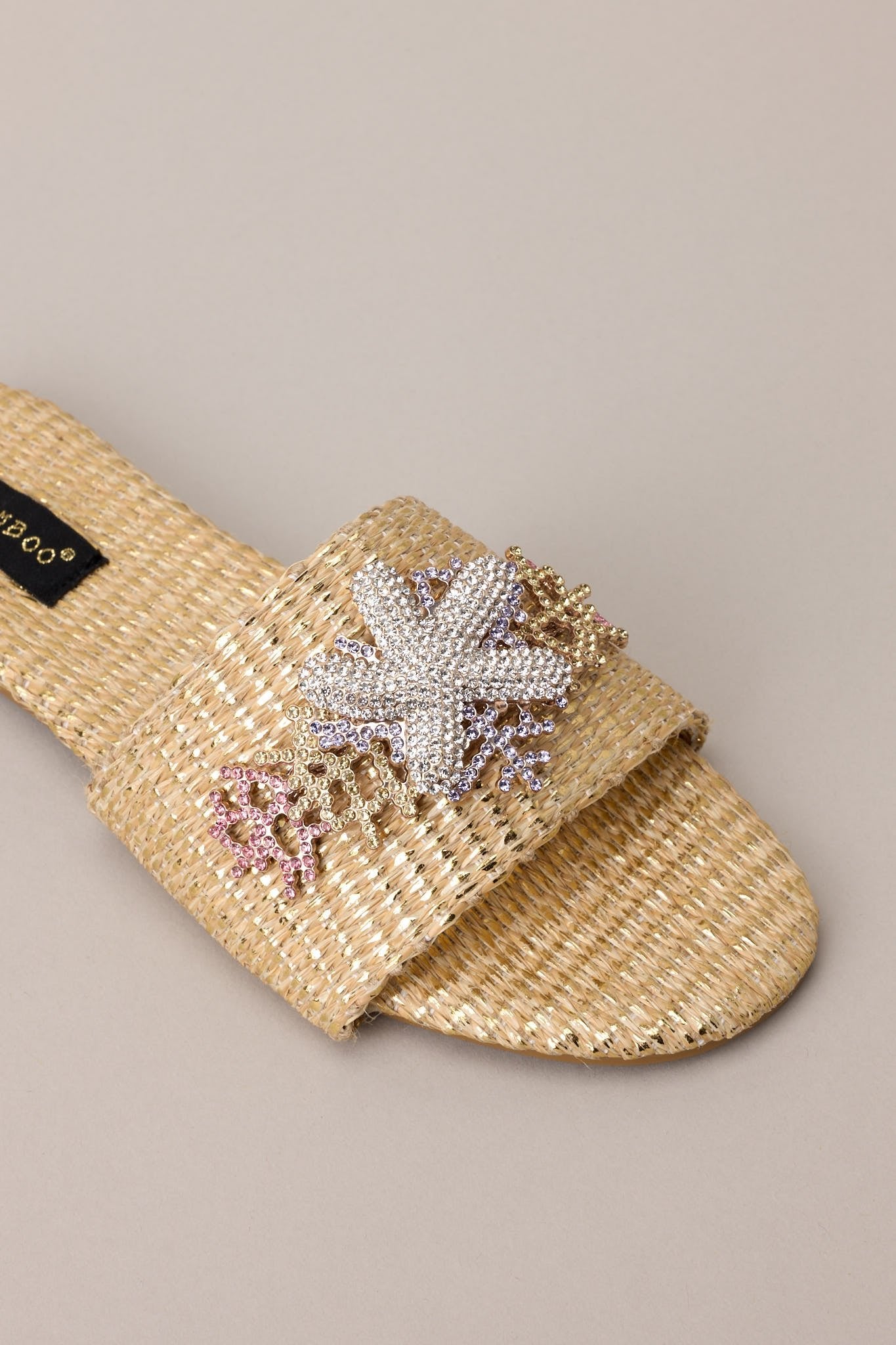 Close up view of the detailing of these sandals that feature a rounded toe, a slip-on design, a wicker-like material, and tropical multicolored rhinestone detailing.