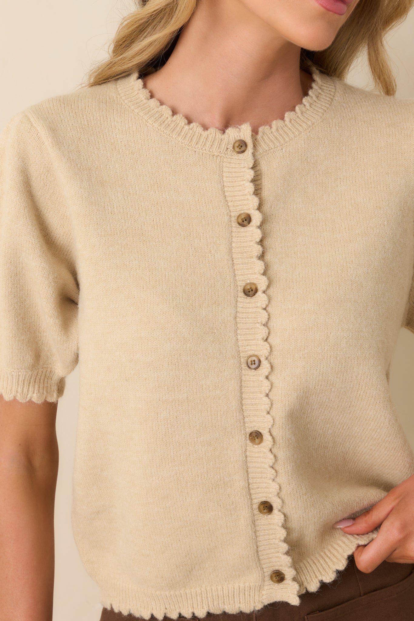 Zoomed-in image capturing the scalloped edges, tortoise shell button texture, and knit fabric detail.