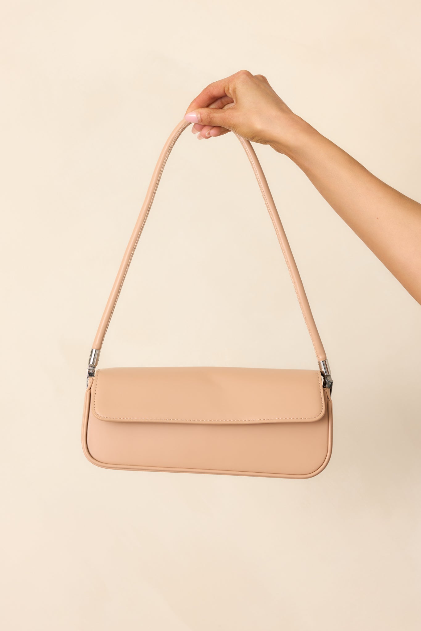 A tan baguette-style handbag featuring a structured shoulder strap, silver hardware, and a sleek silhouette.