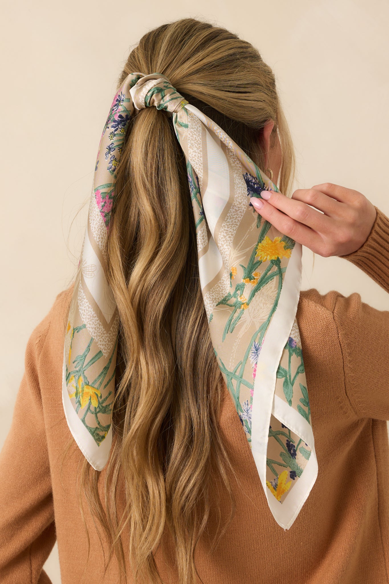 A view from behind of the beige satin scarf with a multicolor floral design and animal print border tied around the hair.