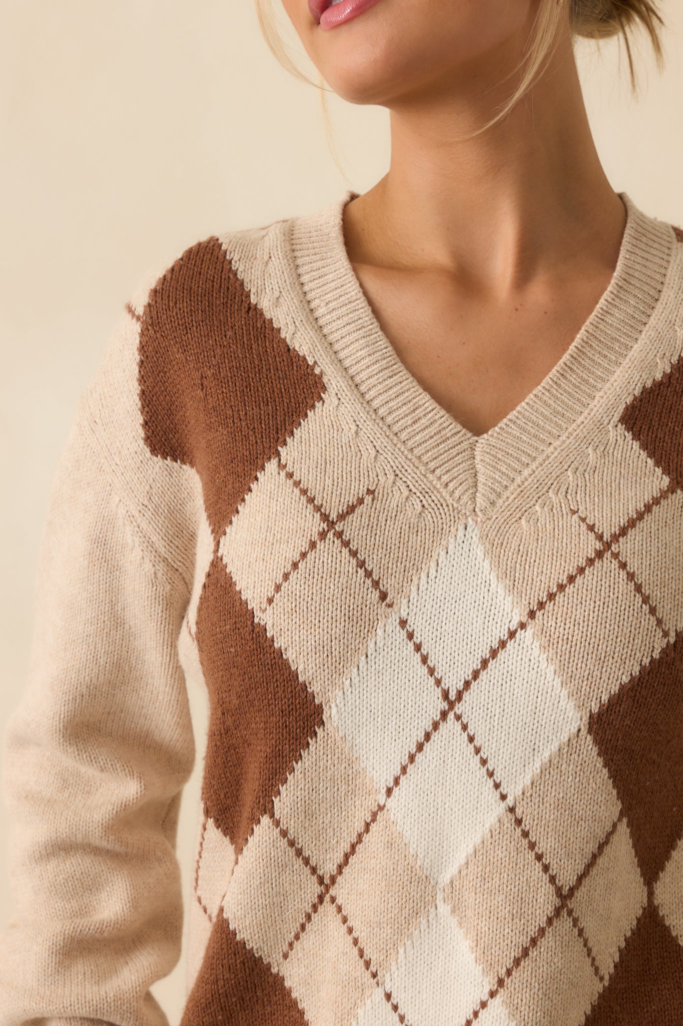 Close-up of the argyle pattern and ribbed hem details on the beige sweater.