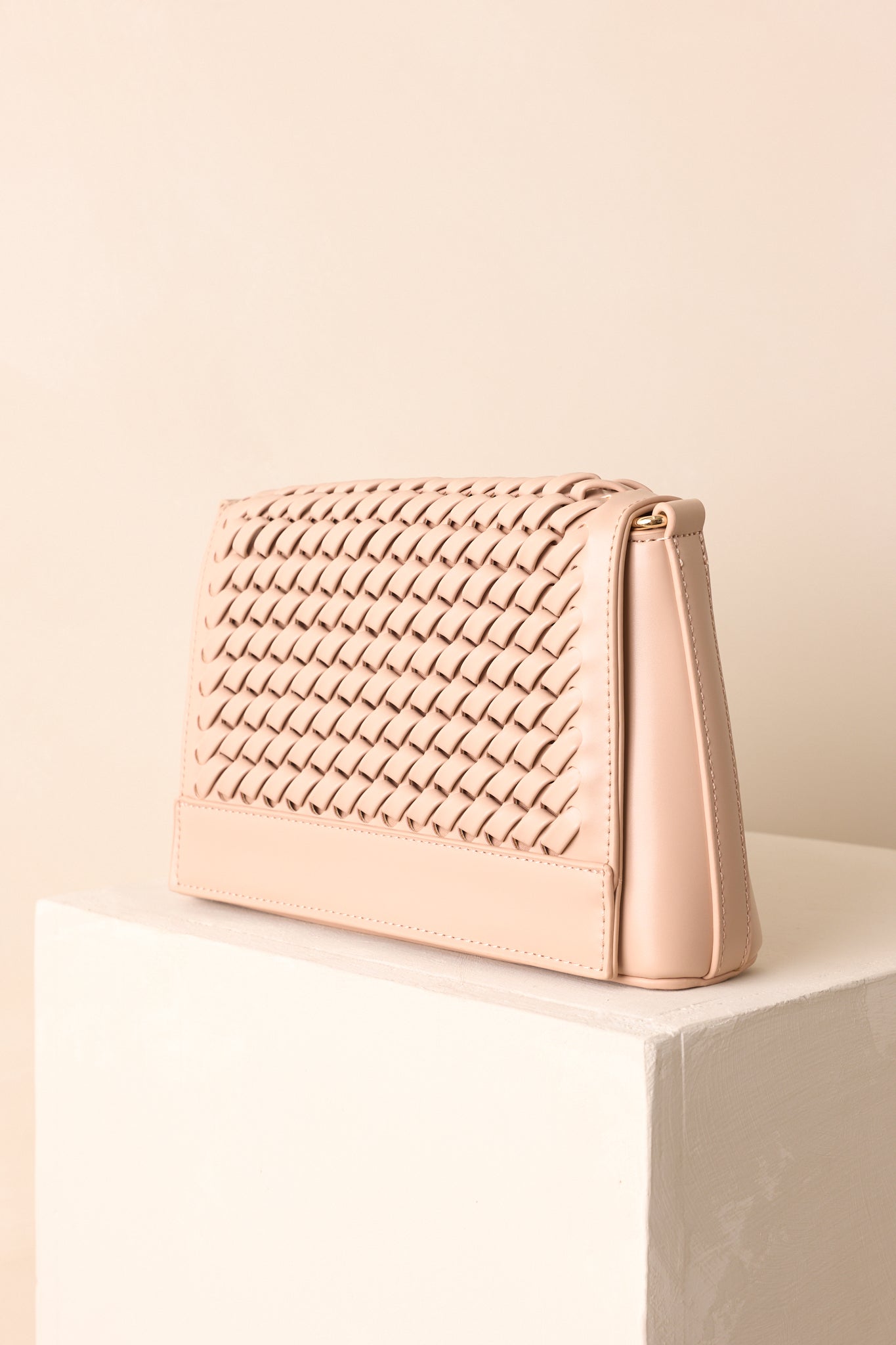 Beige woven handbag highlighting structured shape and adjustable strap attachment.