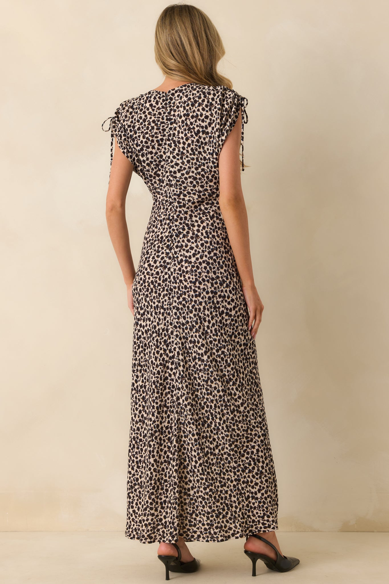 Rear view of black abstract floral print maxi dress with short bow-tied sleeves and hidden zipper closure.