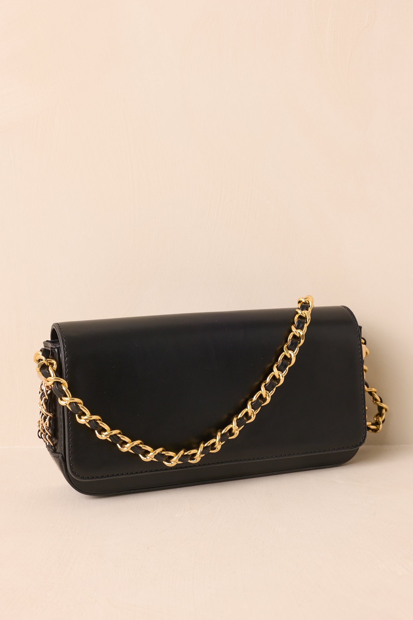 Cropped view focusing on the magnetic flap closure and smooth black faux leather material of the handbag.