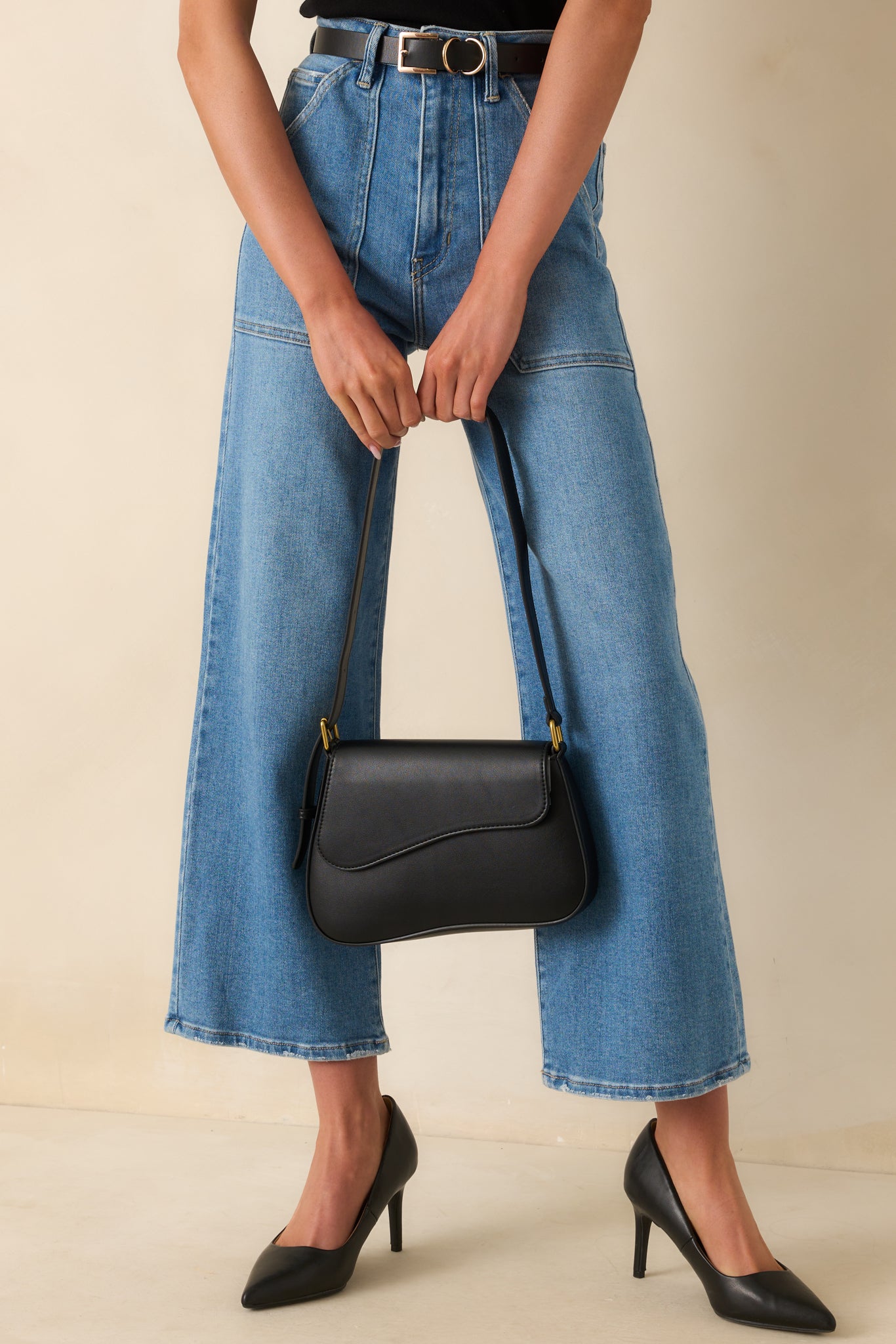 Front-facing full body view of the black saddlebag showing the curved flap-front silhouette, adjustable shoulder strap, and gold-tone hardware.