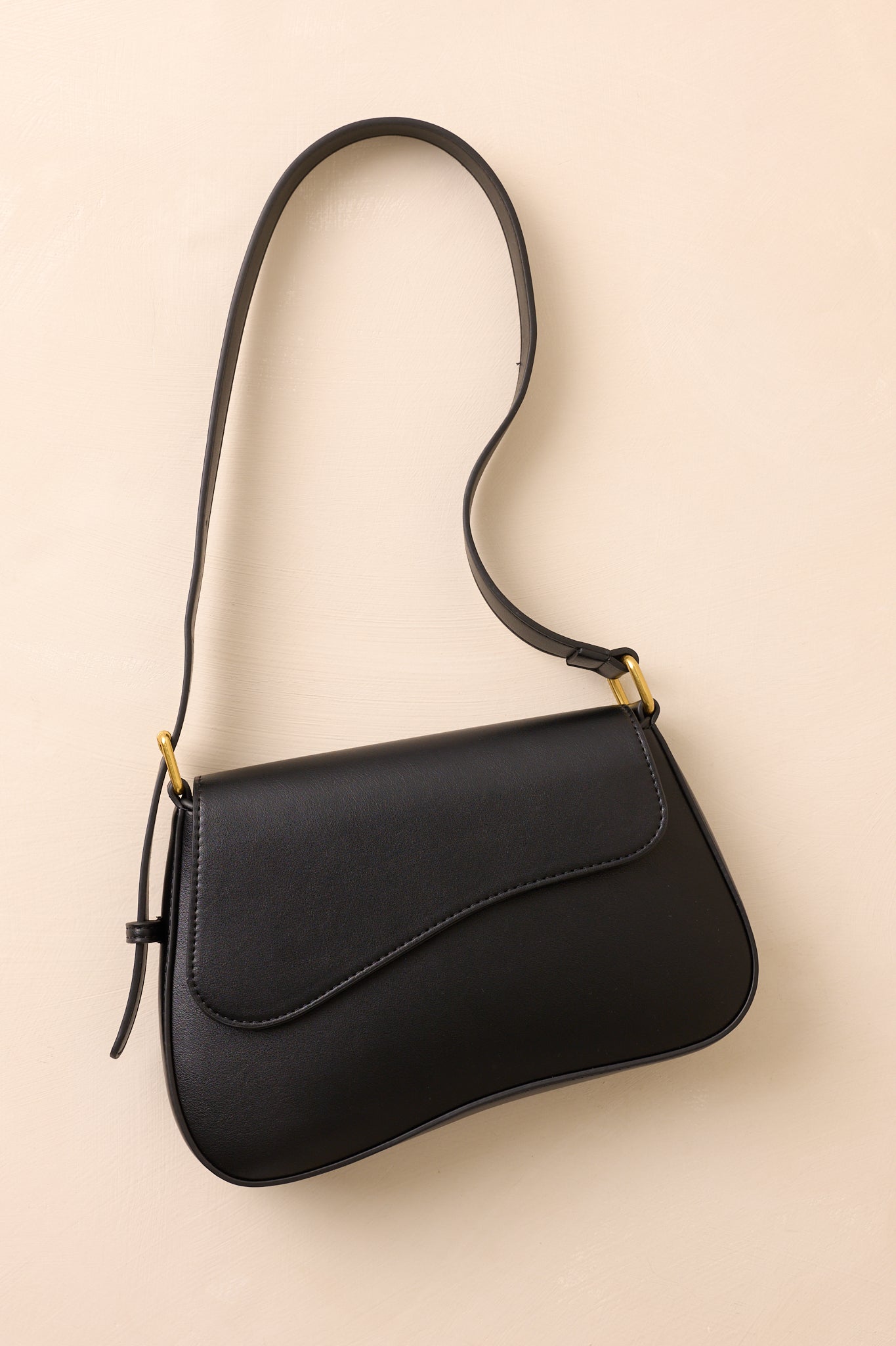 A complete view of the black saddlebag featuring its adjustable shoulder strap and structured saddle shape.