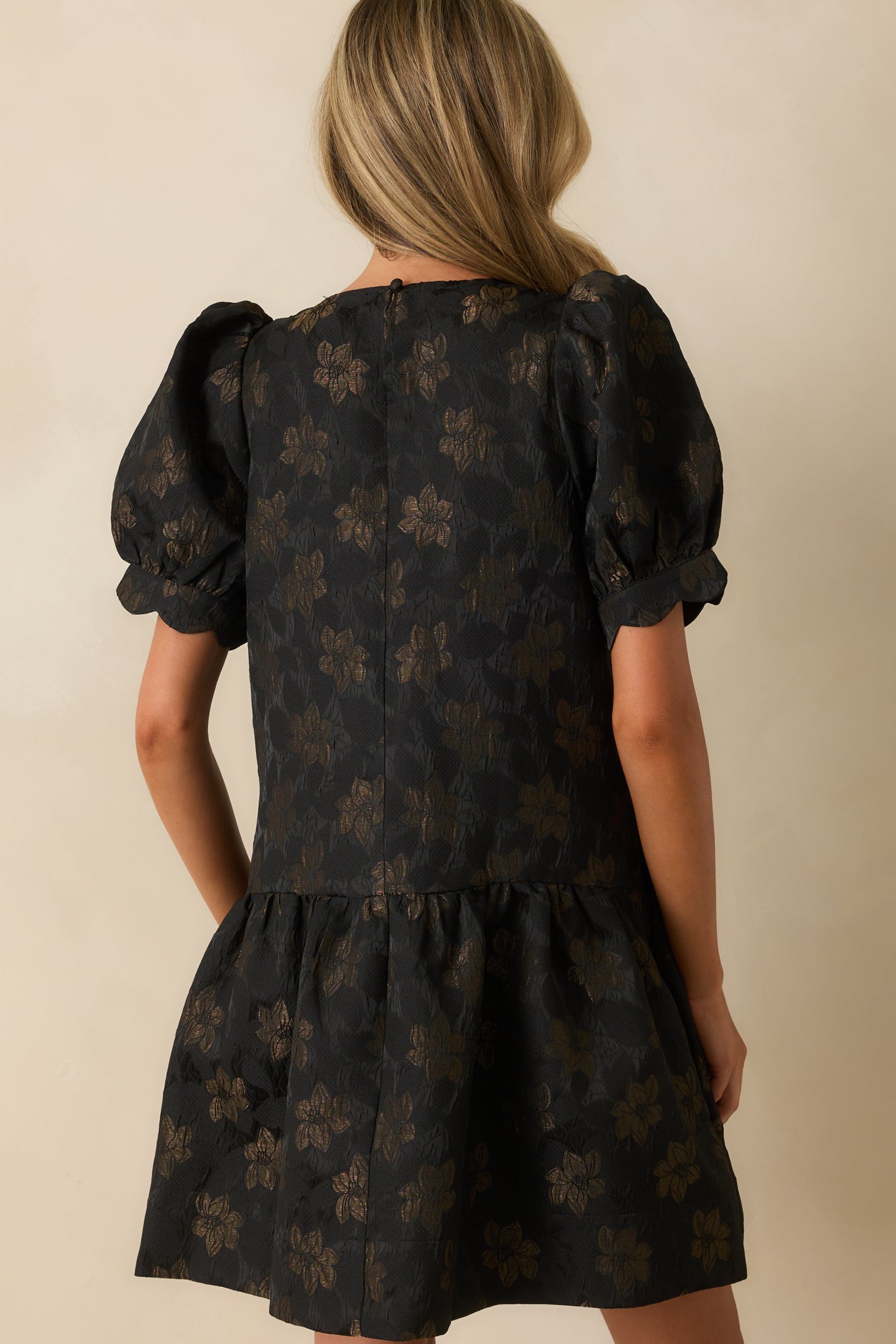 Rear view of the black mini dress showing short sleeves, tiered skirt, and smooth fabric.