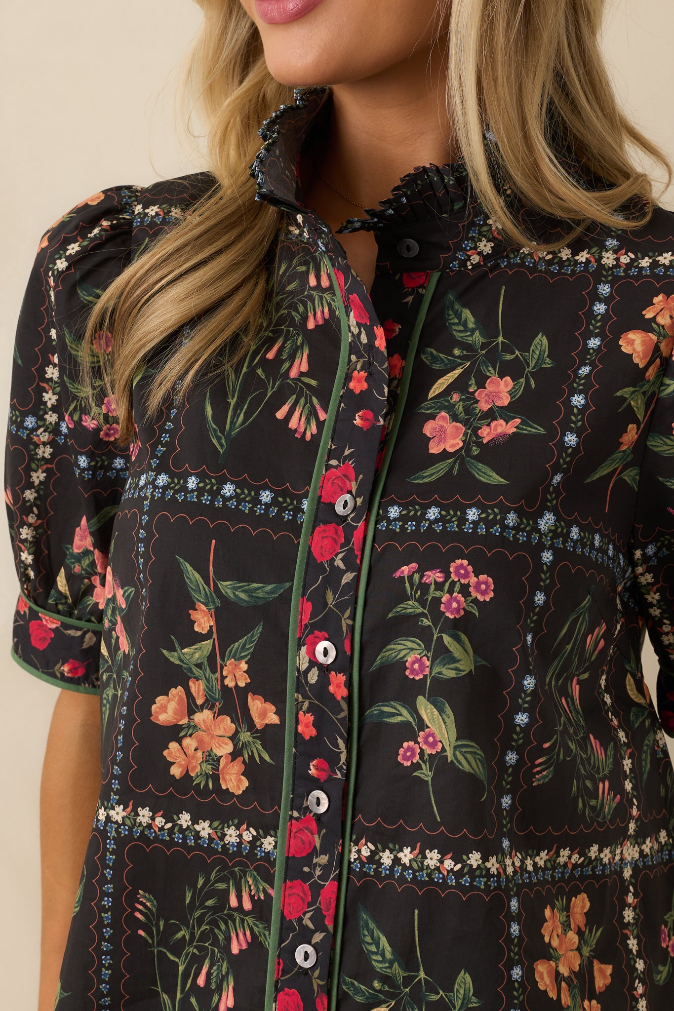 A close-up detail of the pleated ruffle collar with green trim on the black patchwork floral print top.