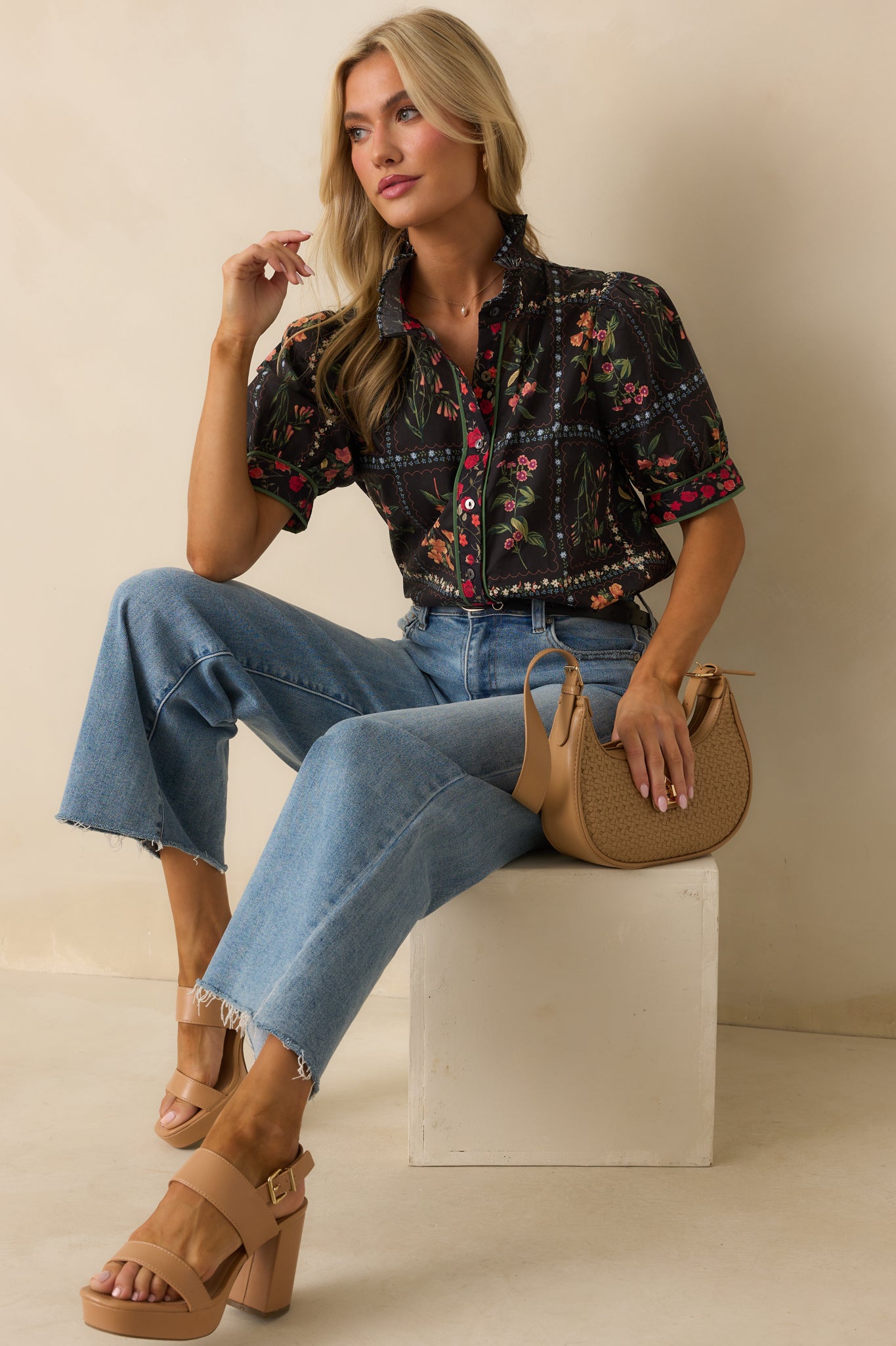 The black floral patchwork top shown front facing with a button front design and green trim accents.