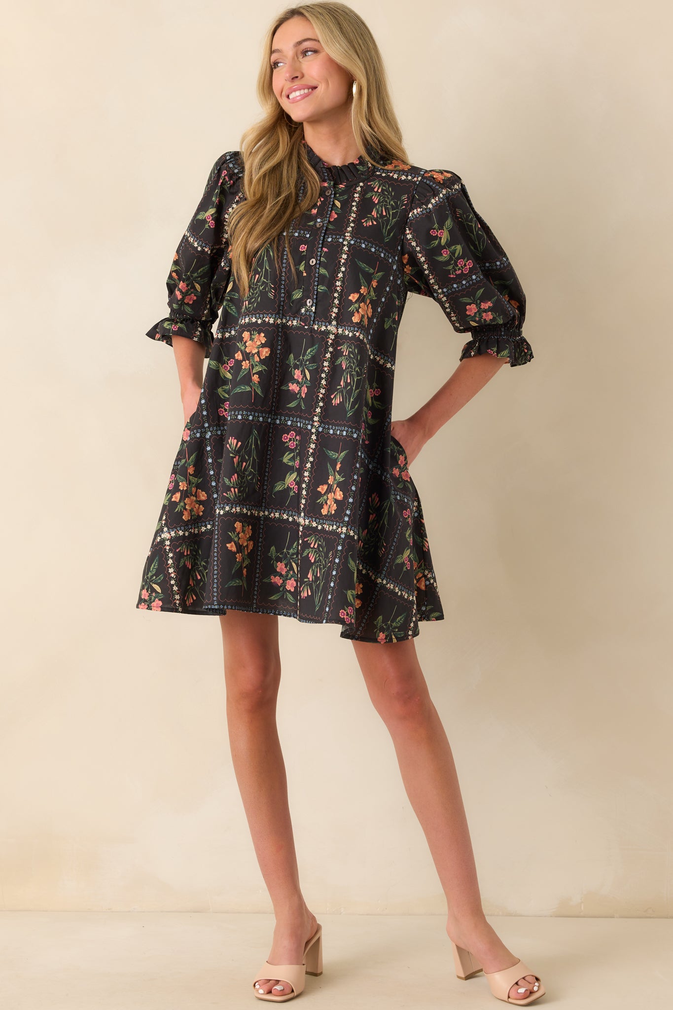 A front full body view of the black mini dress featuring an orange floral block print and high ruffle-trimmed neckline.