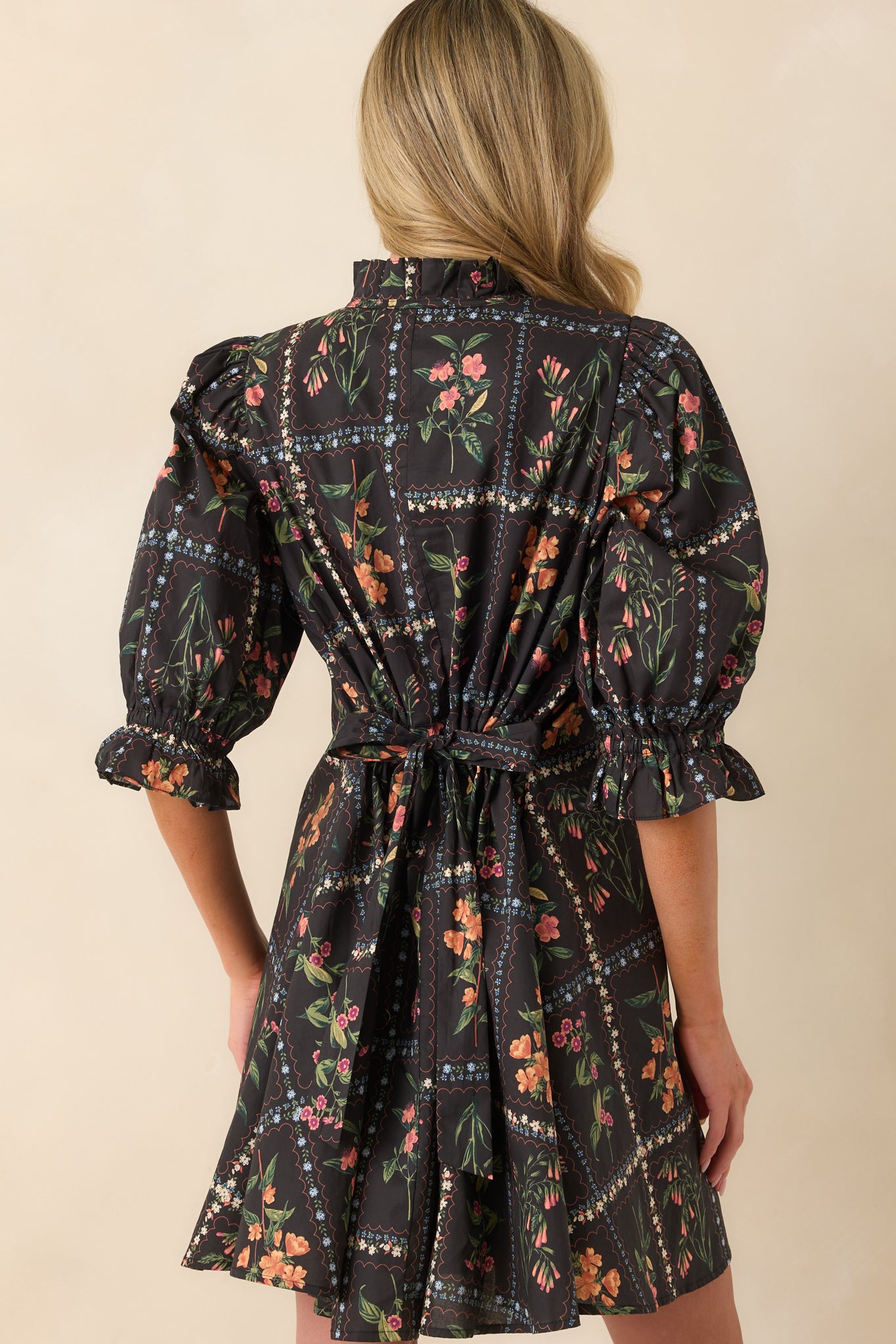 A back view of the black mini dress displaying the continuation of the floral block print and the silhouette of the puff sleeves.