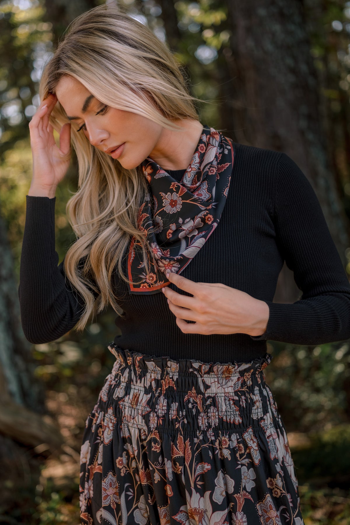 Model wearing a black ribbed long-sleeve top with a floral neck scarf and a matching smocked-waist floral skirt.