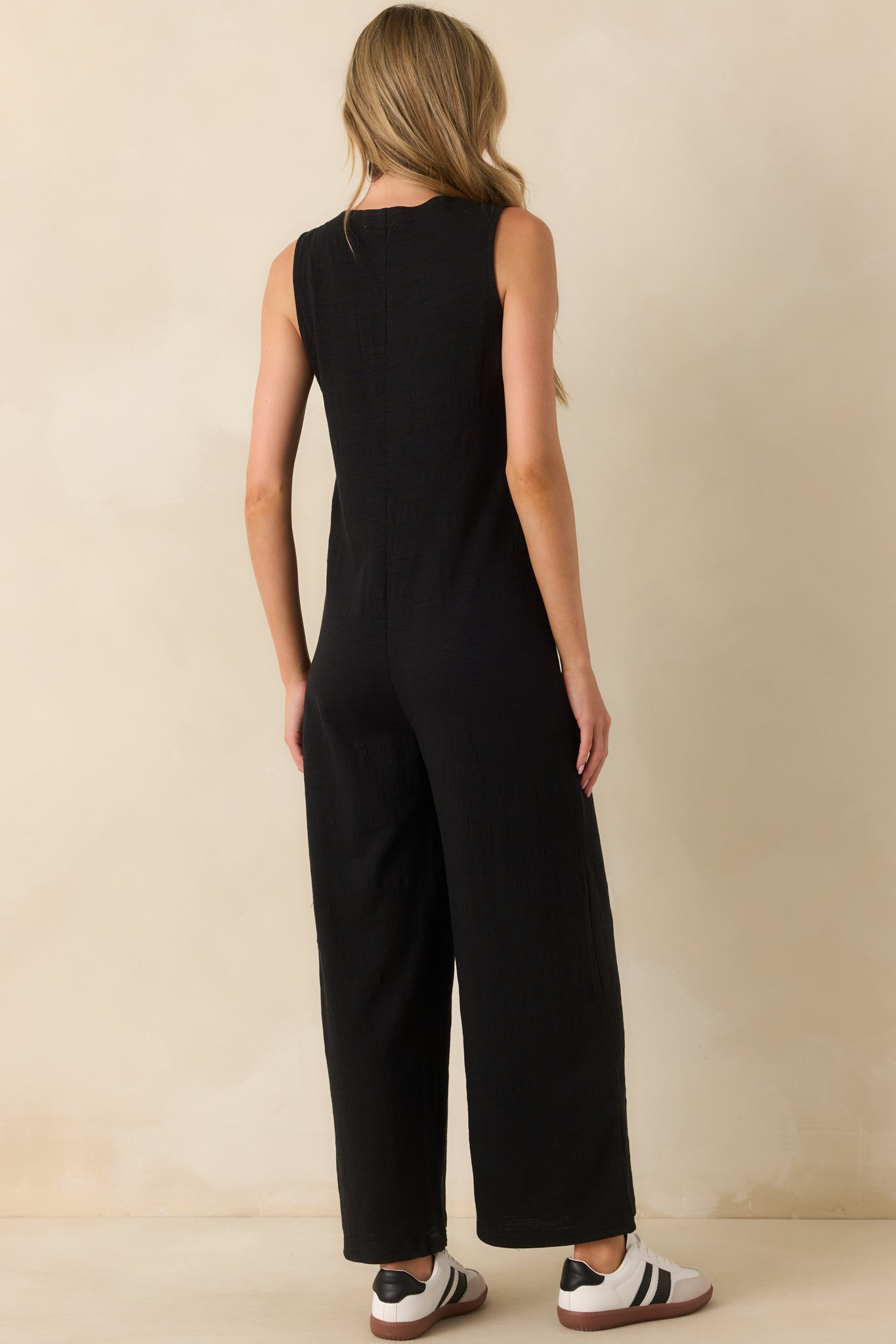 Back view of the sleeveless black jumpsuit featuring wide legs and lightweight textured fabric.