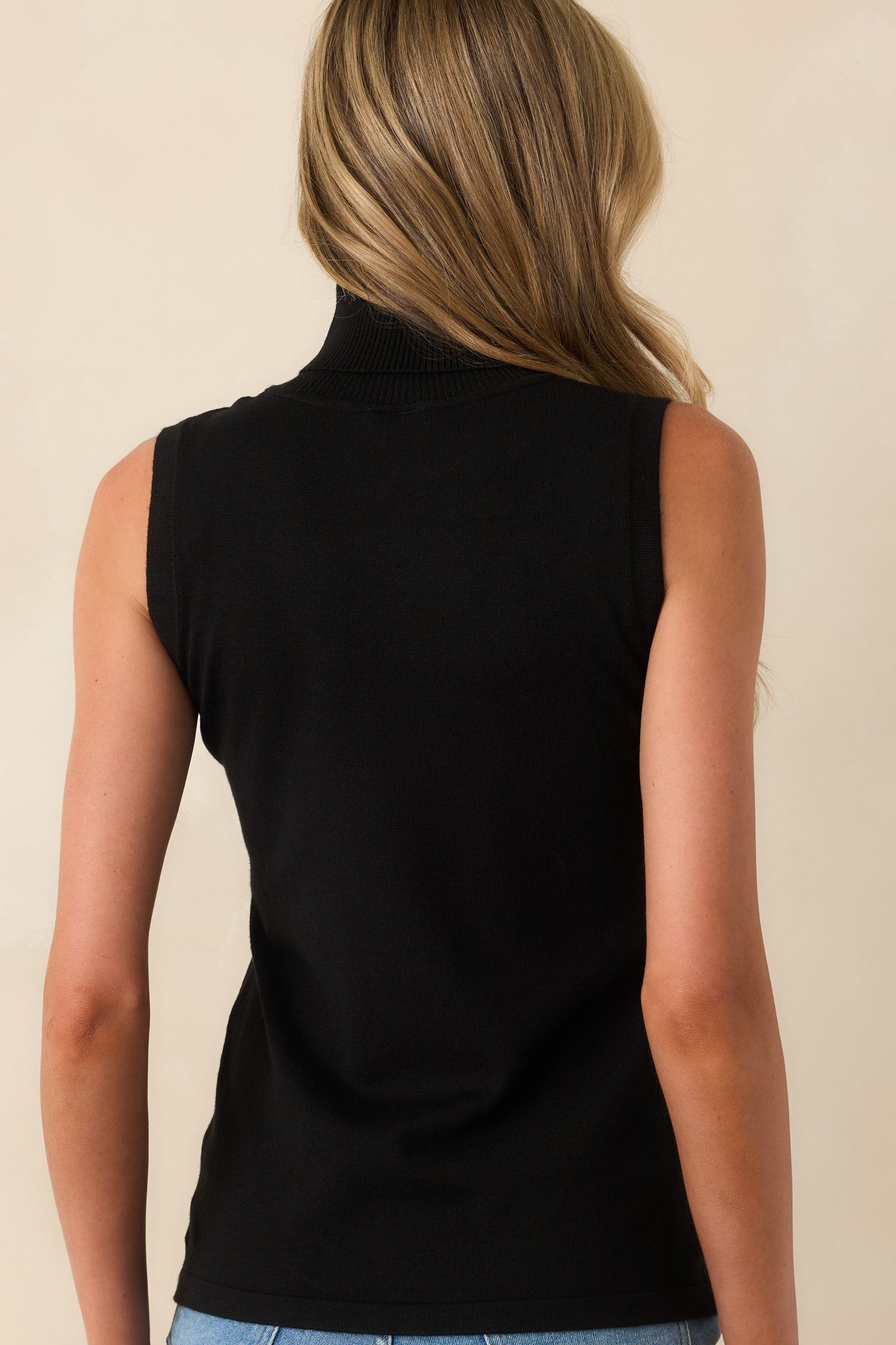 A view from behind showing the sleeveless shape, rolled turtleneck, and consistent ribbed texture across the back of the sweater.