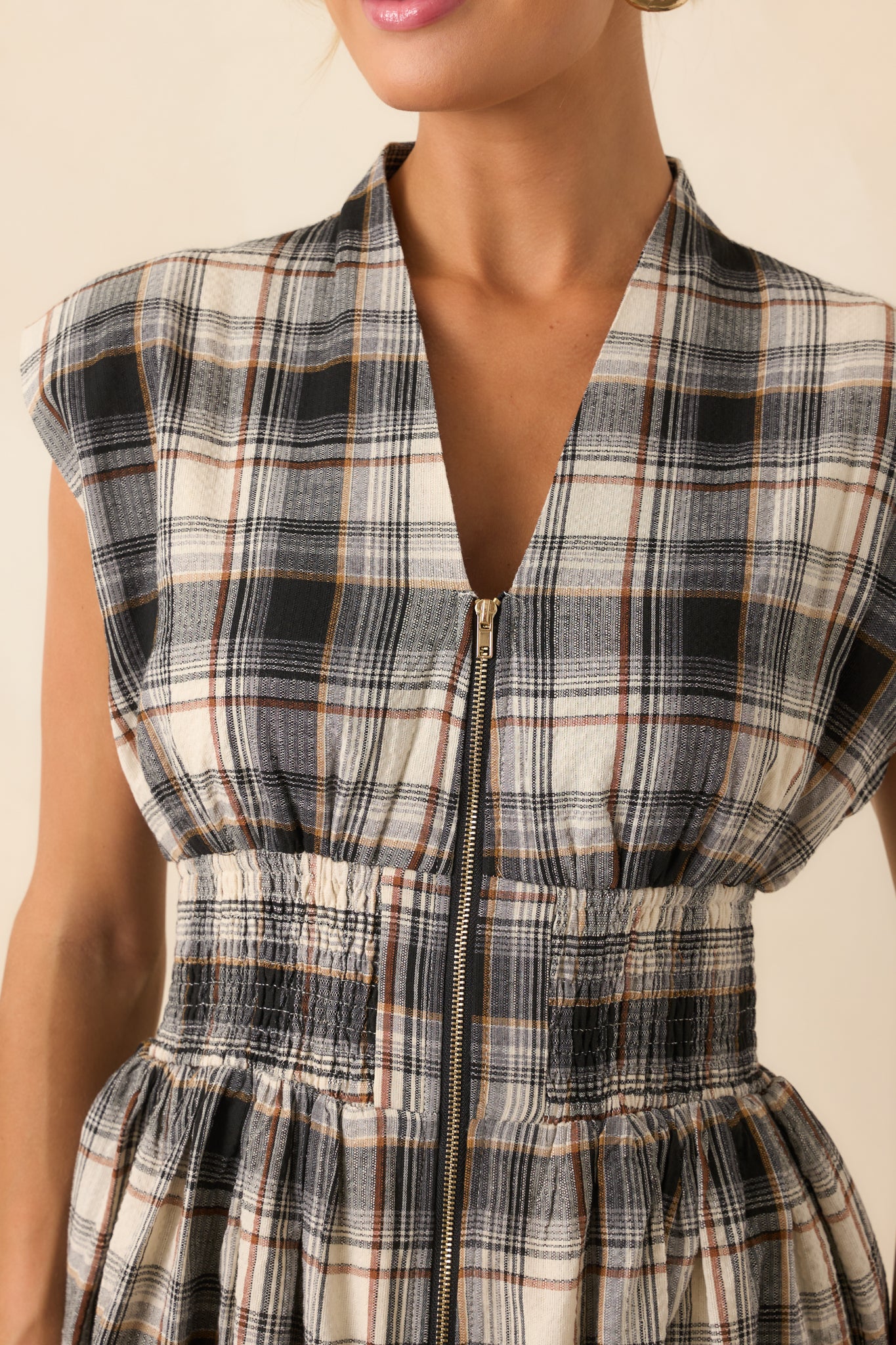 Close-up of the black tartan plaid fabric and front zipper detail, showing the smocked waistband and subtle texture.