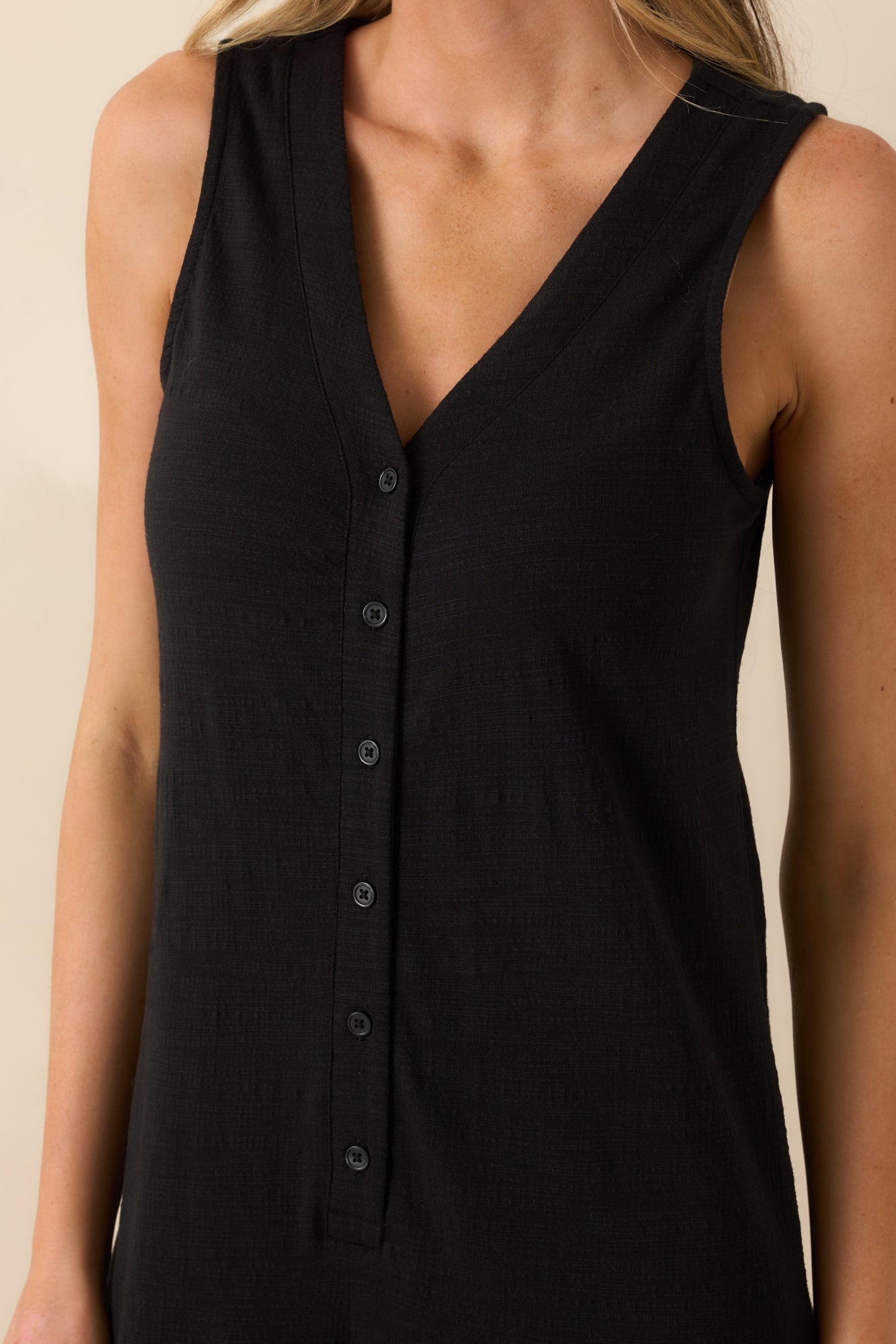 Close-up detail of the v-neckline and functional button front bodice on the black textured jumpsuit.