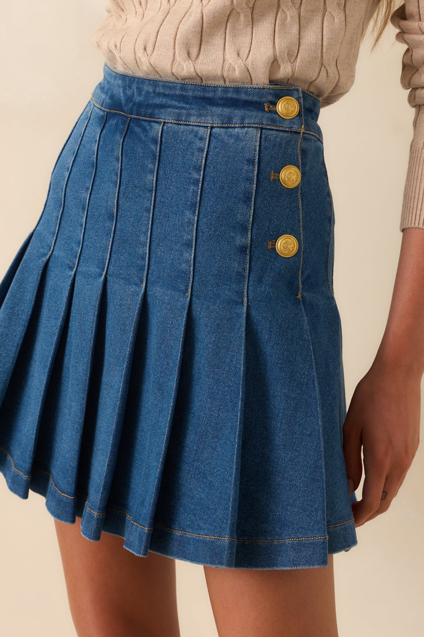 Close-up of one side of the skirt showing the detailed embossing on the gold buttons and the grain of the denim fabric.