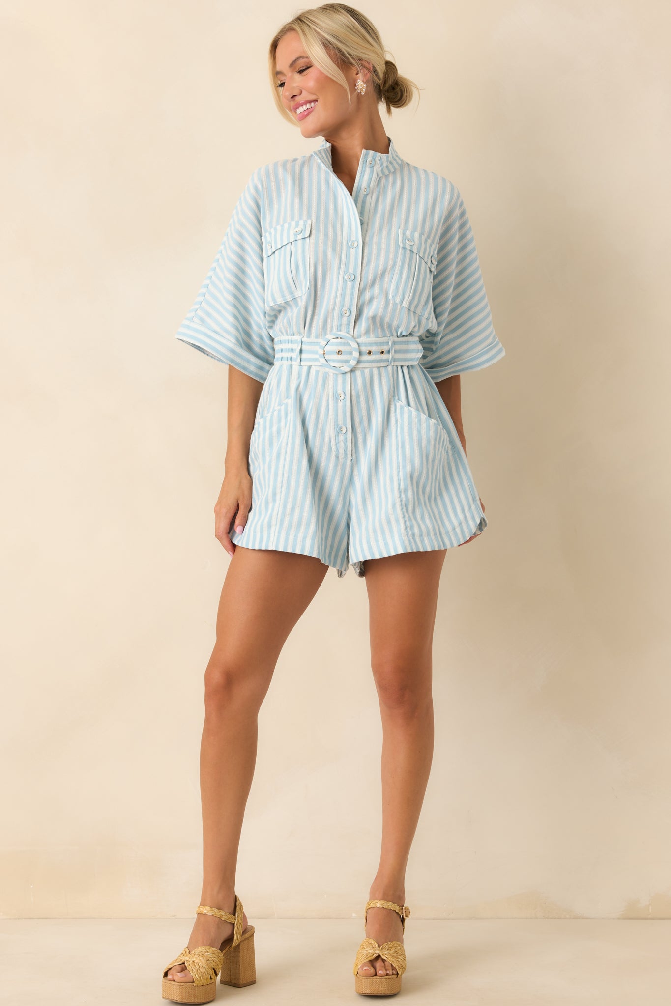 Full view of light blue striped romper featuring a collared neckline, button front, cuffed short sleeves, belted waist, and front patch pockets.