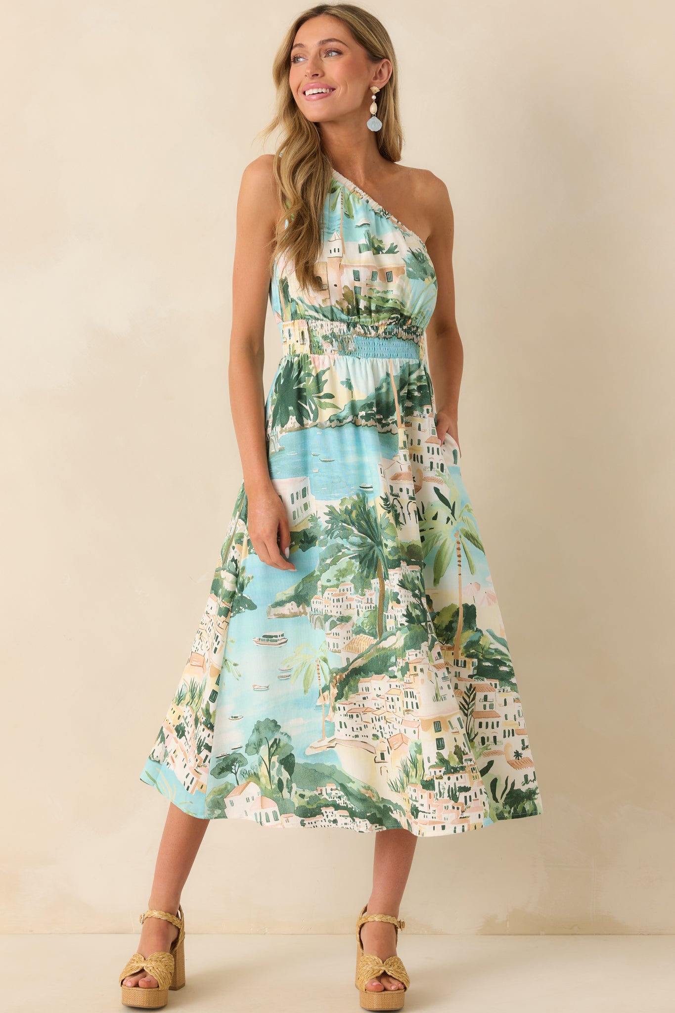 Front-facing full view of the midi dress featuring a blue watercolor-style shoreline print, elastic one-shoulder neckline, and soft drape.