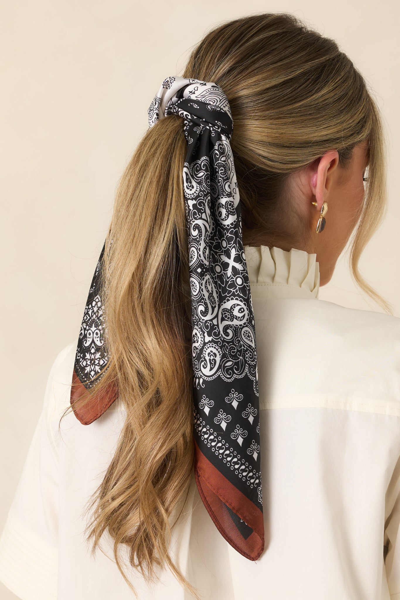Brown, black, and ivory paisley bandana scarf styled as a ponytail hair scarf with a patchwork paisley print.