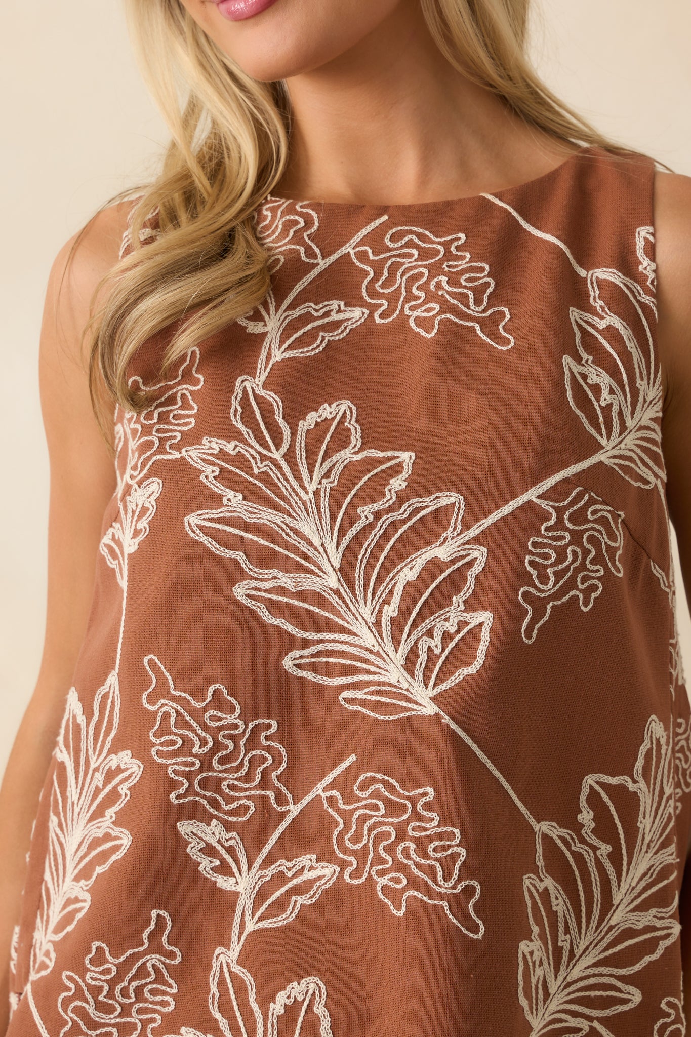 Detailed embroidery view showing ivory floral stitching on the brown fabric.