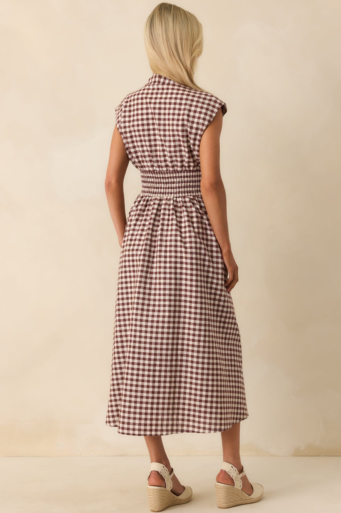A view from behind showing the brown gingham midi dress with capped sleeves and fitted smocked waist.