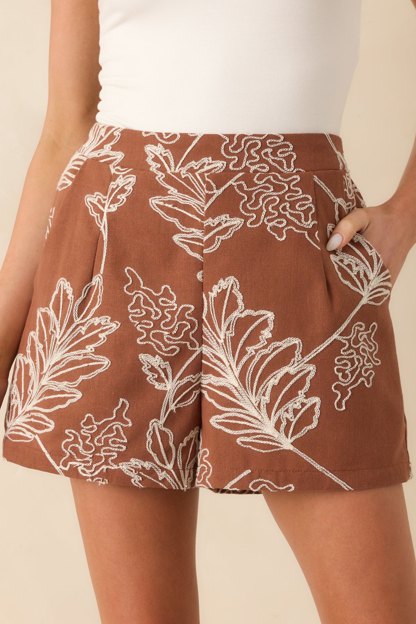 Close-up of the embroidery and fabric texture, capturing the ivory floral stitching and fine detailing on the brown fabric.