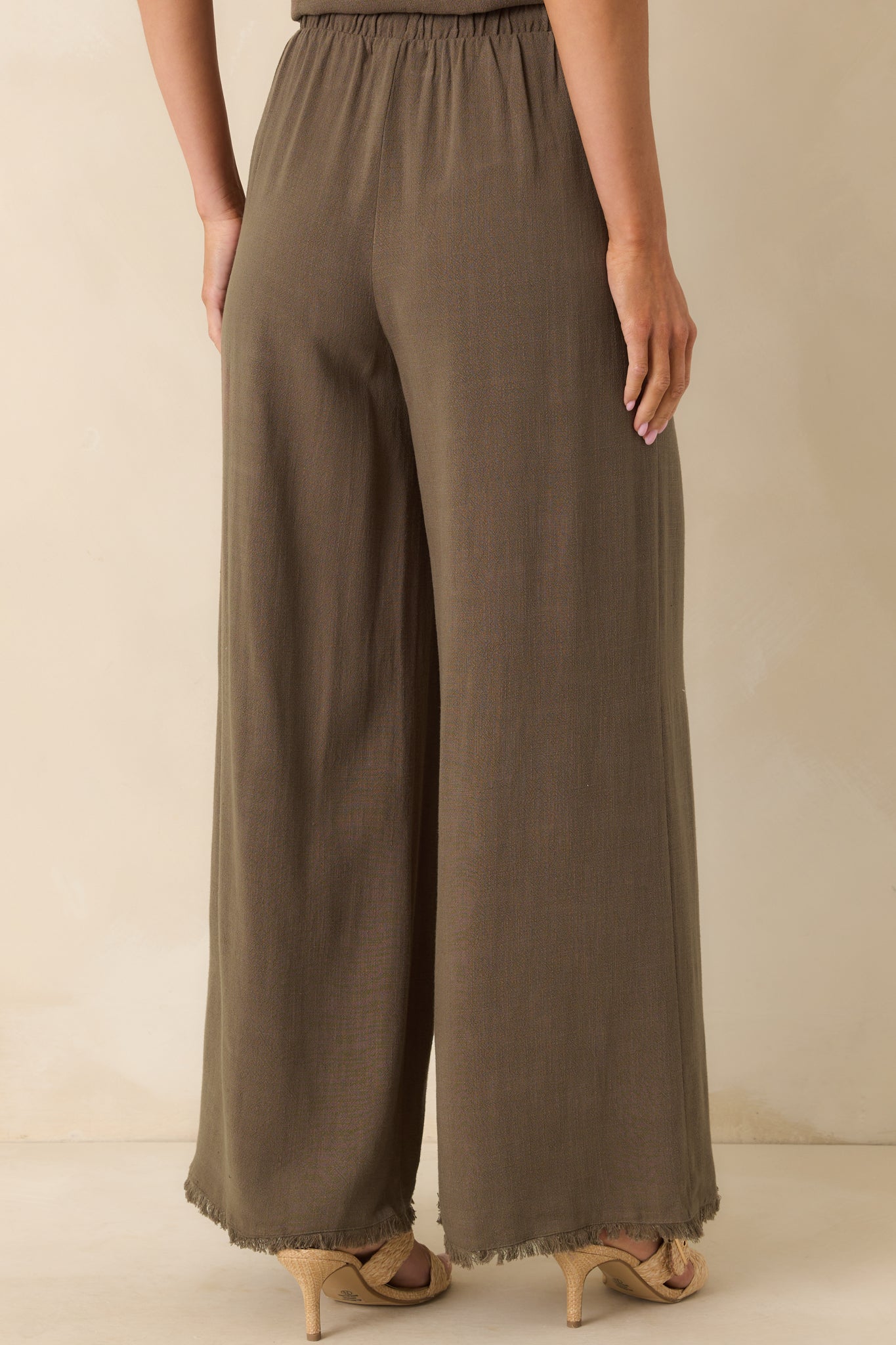 A view from behind of the tiki brown pants showing the elastic high rise waistband, functional pockets, and wide leg flow.