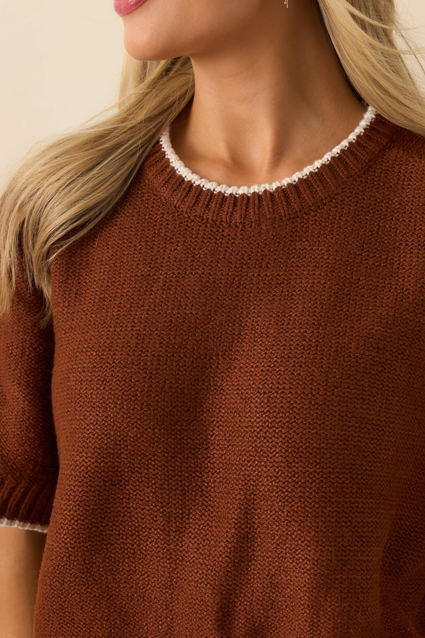 Detailed look at the knit texture and ivory trimmed crew neckline of the brown sweater.