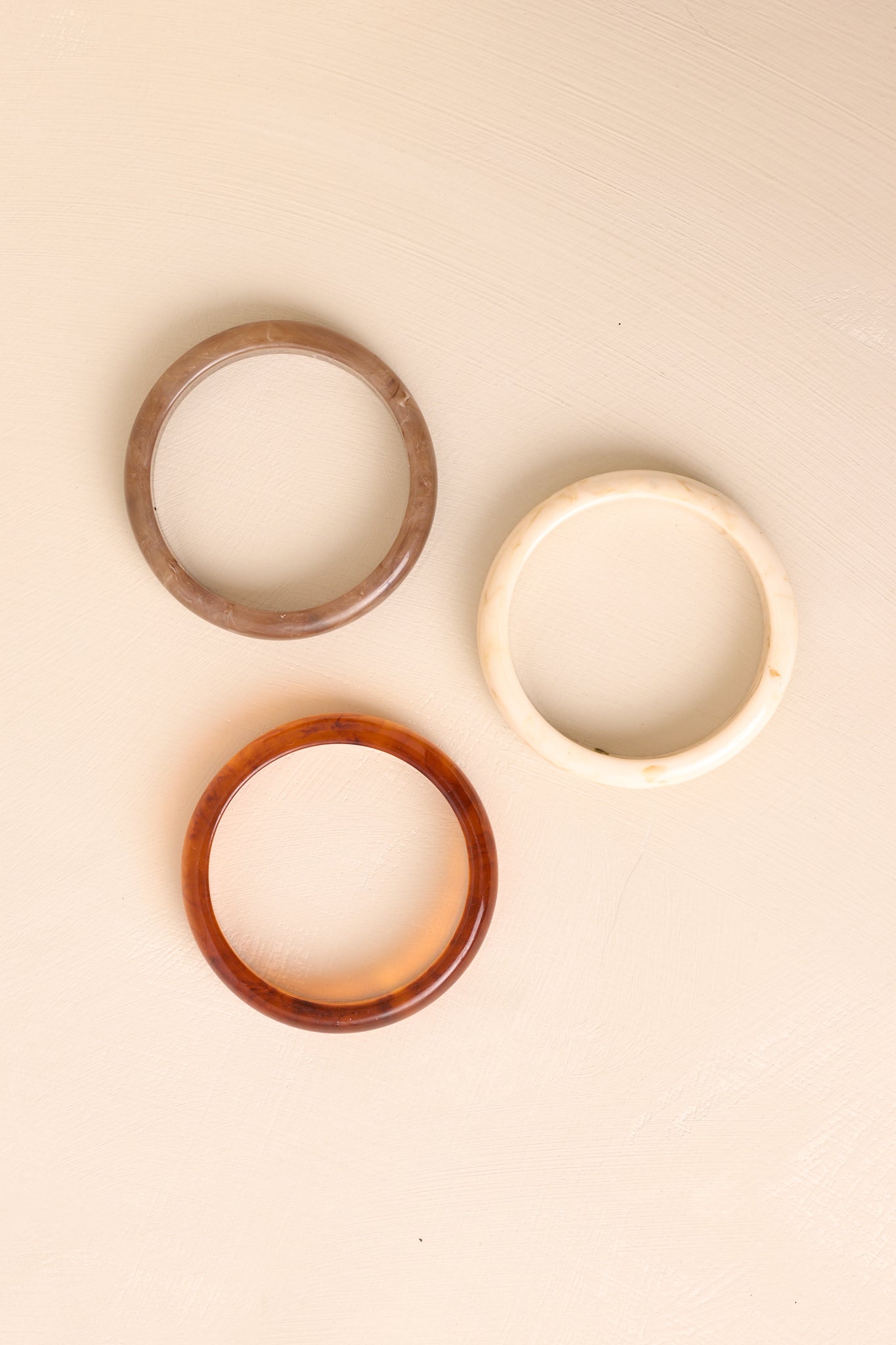 The trio of marbled bangle bracelets shown against a beige background, highlighting the mixed neutral tones.
