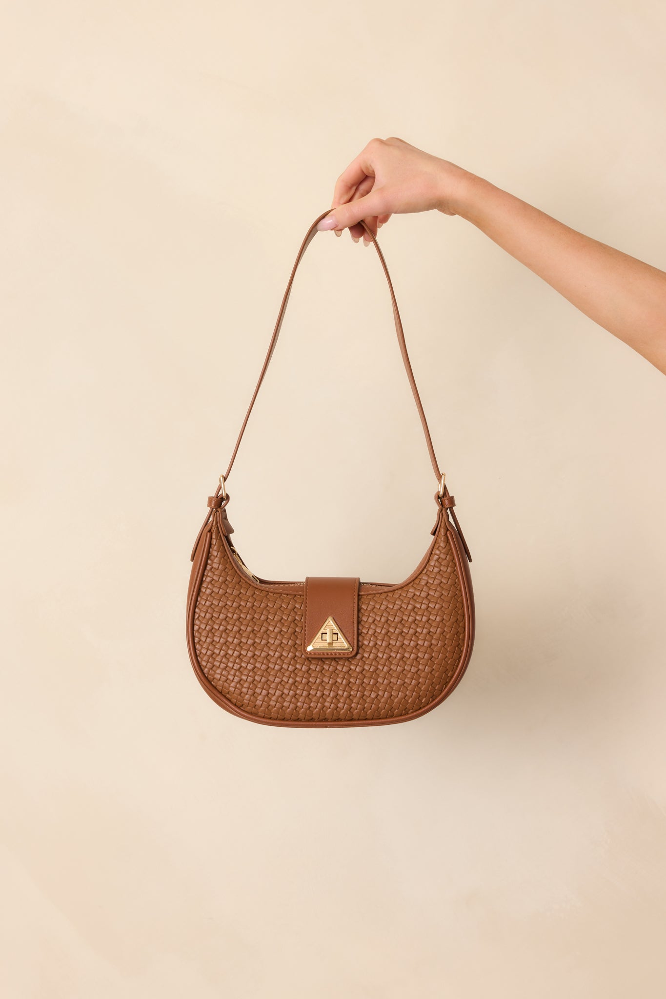 Front-facing full view of the cognac brown shoulder bag showing the curved half-moon shape, woven faux leather texture, and gold triangular twist-lock flap closure.