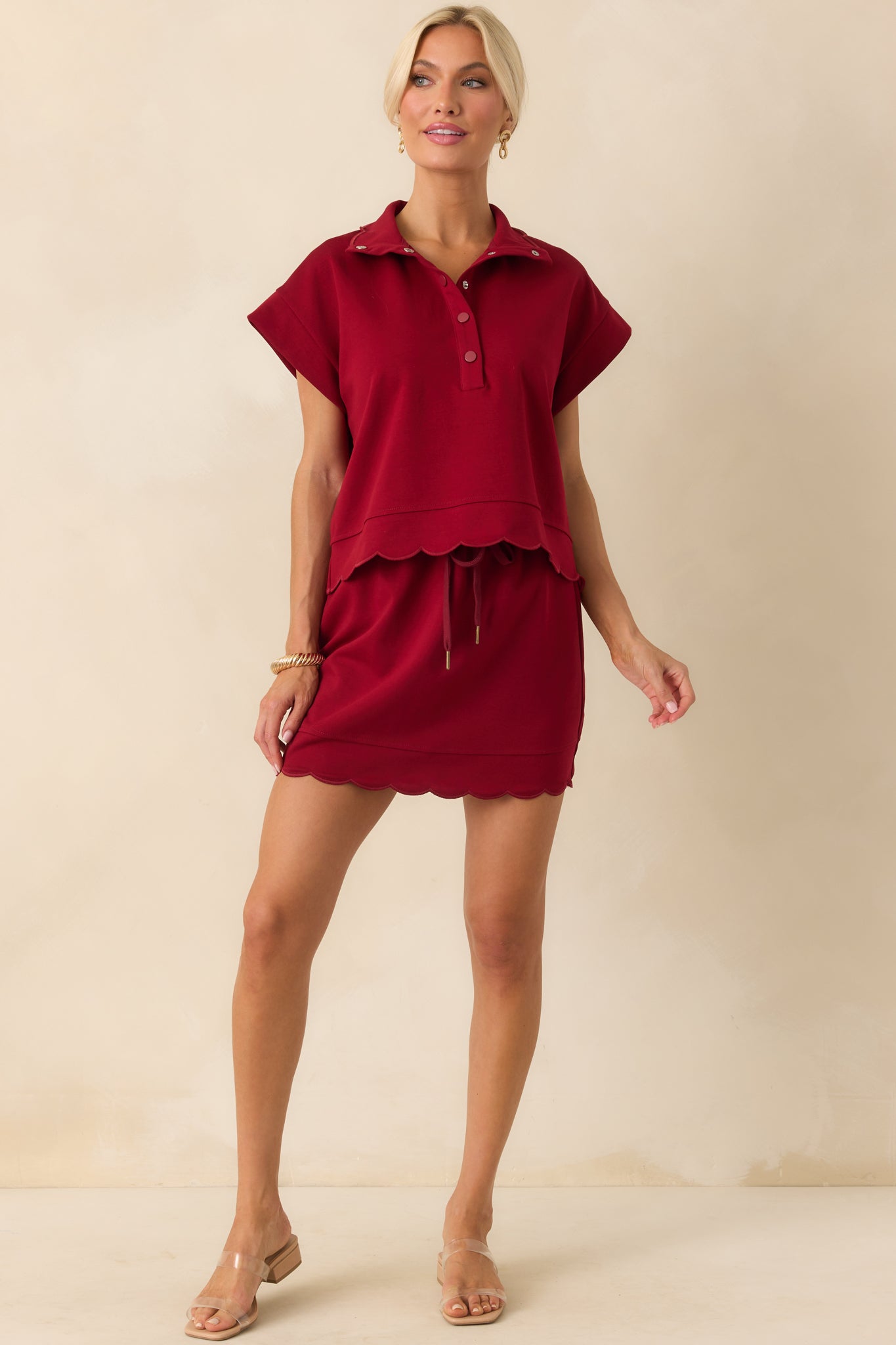 A full body shot emphasizing the embroidered scallop hems along the sleeves and lower edge.