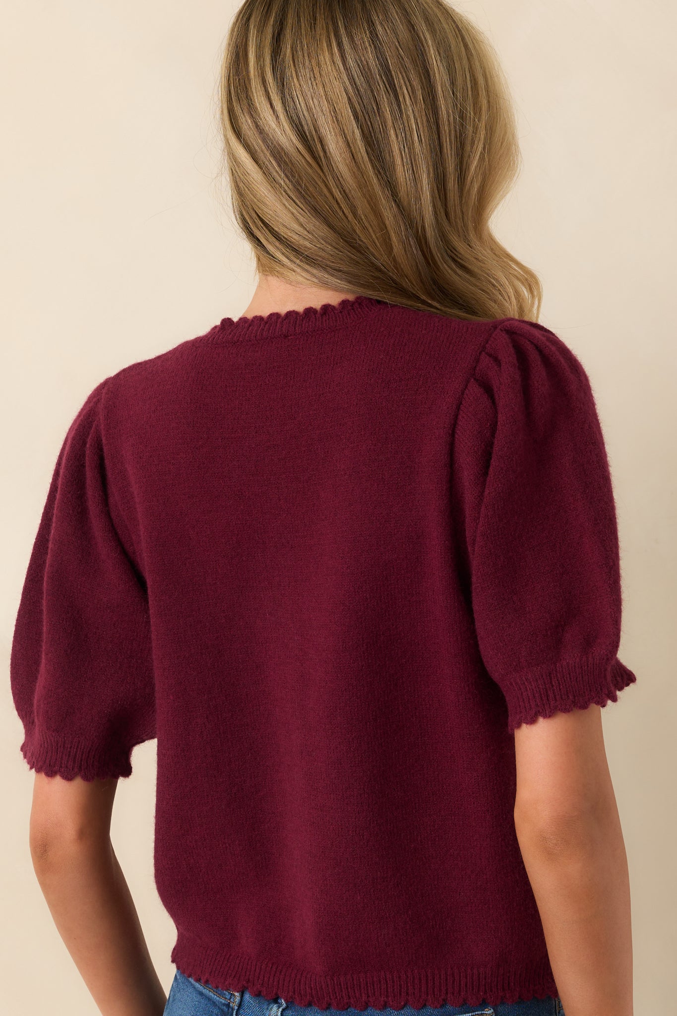 A view from behind showing the smooth knit fabric, short sleeves, and ribbed hemline of the wine red cardigan.