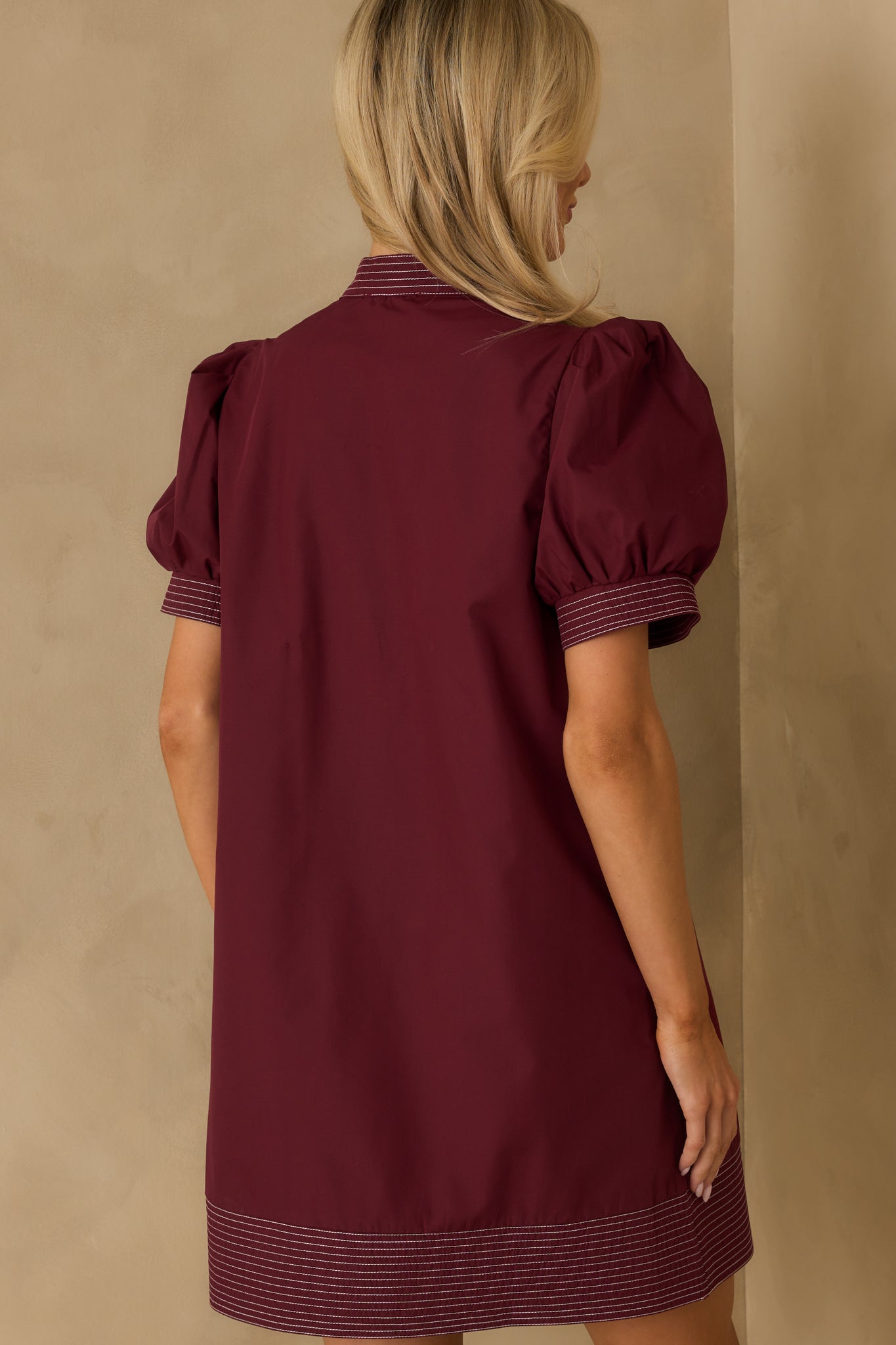 Rear view of burgundy mini dress with puff sleeves and stitched trim accents.