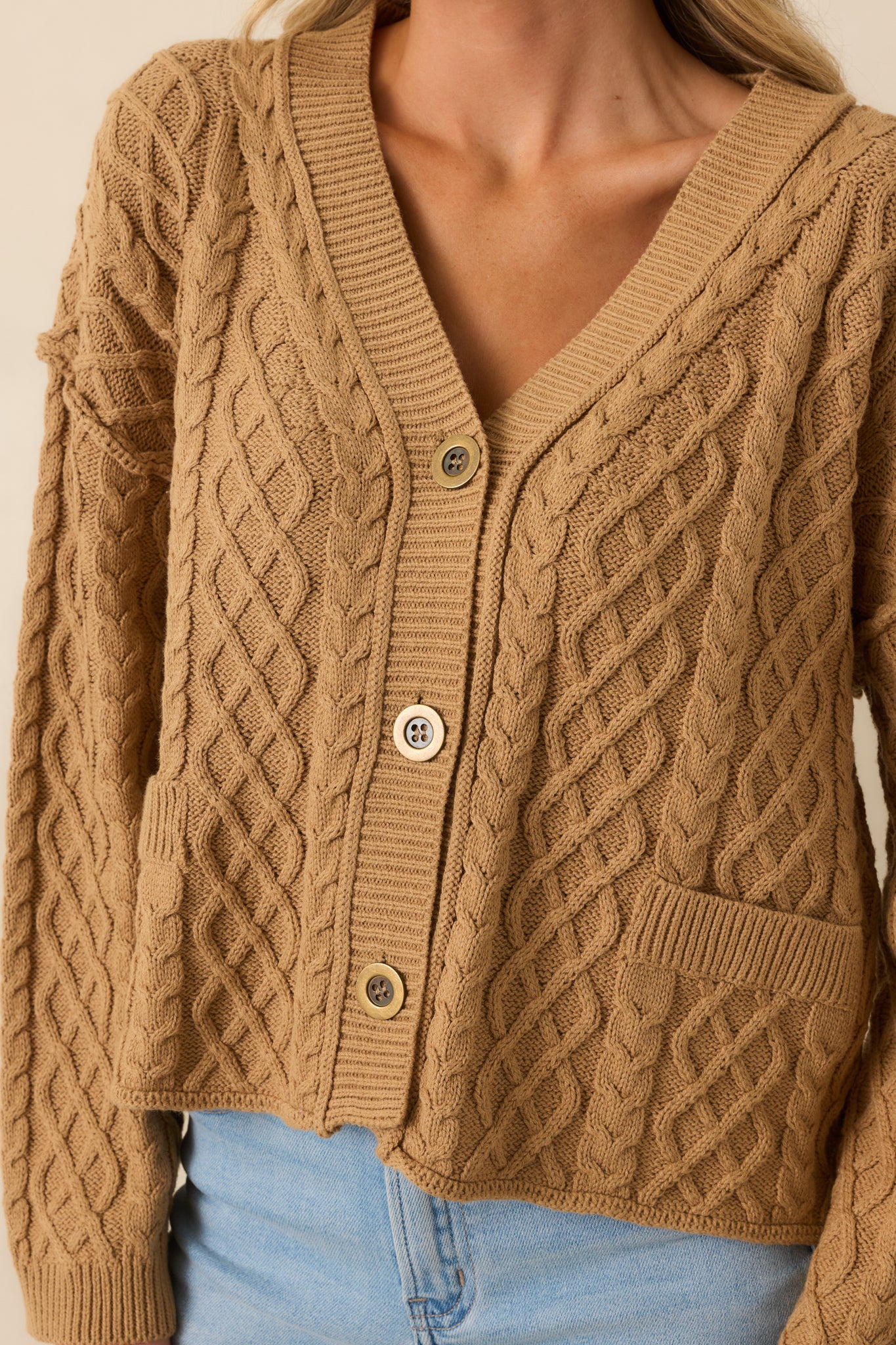 Close-up detail of the camel cable knit texture and stitching on the cardigan.