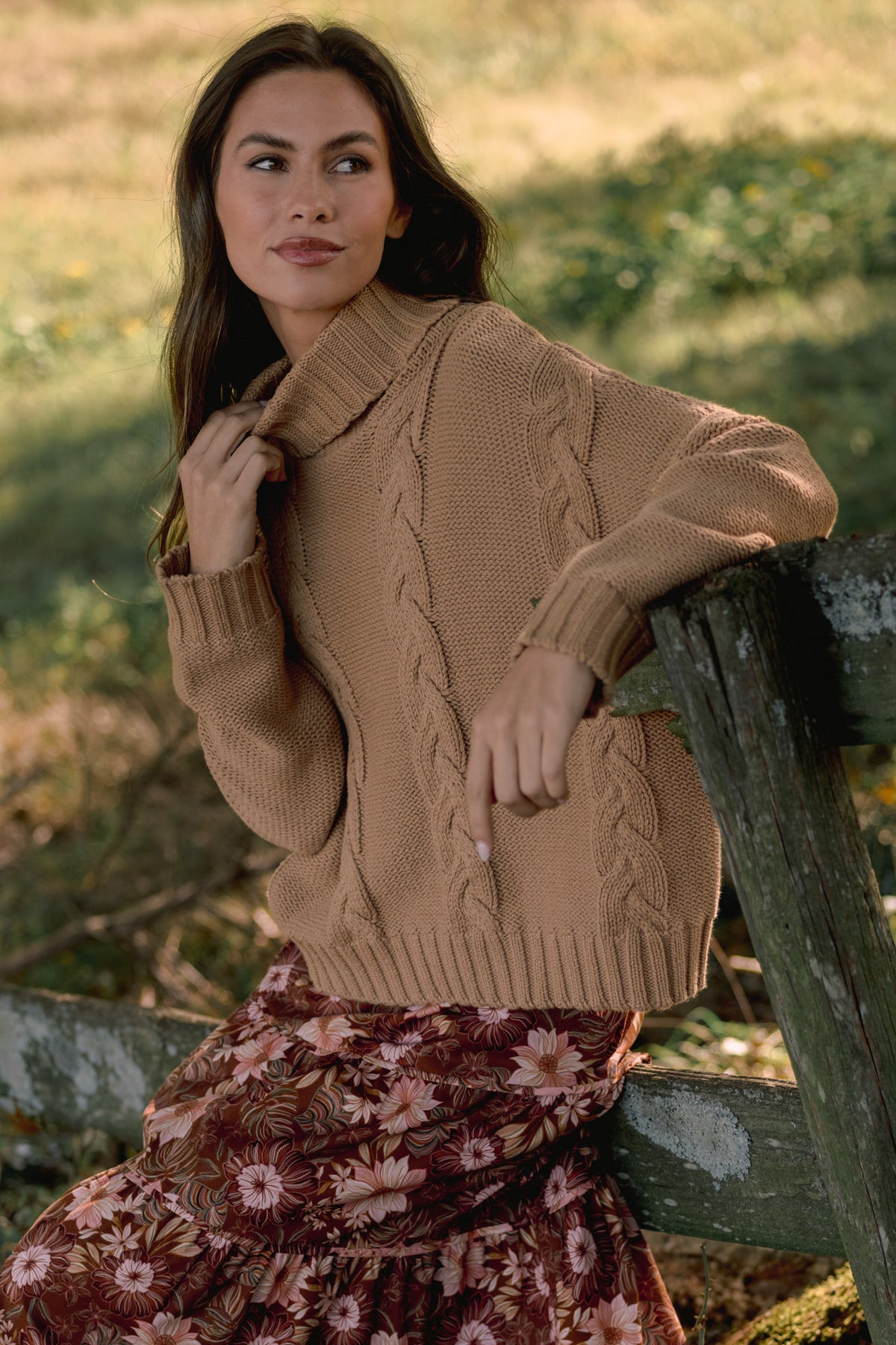 Model wearing a camel cable-knit turtleneck sweater with long sleeves, ribbed cuffs, and a ribbed hem.