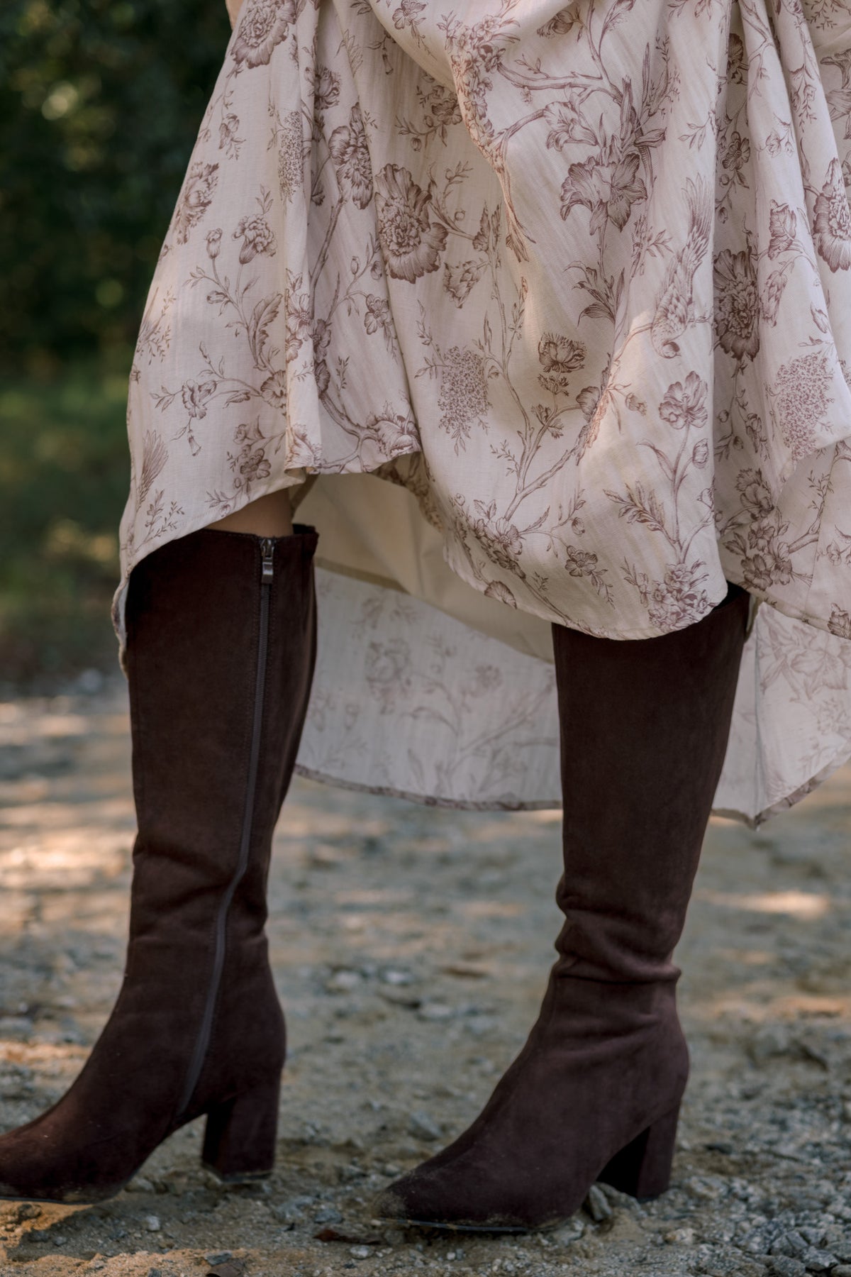 Close-up of chocolate brown knee-high boots with pointed toes, block heels and side zippers, styled with a cream floral skirt.